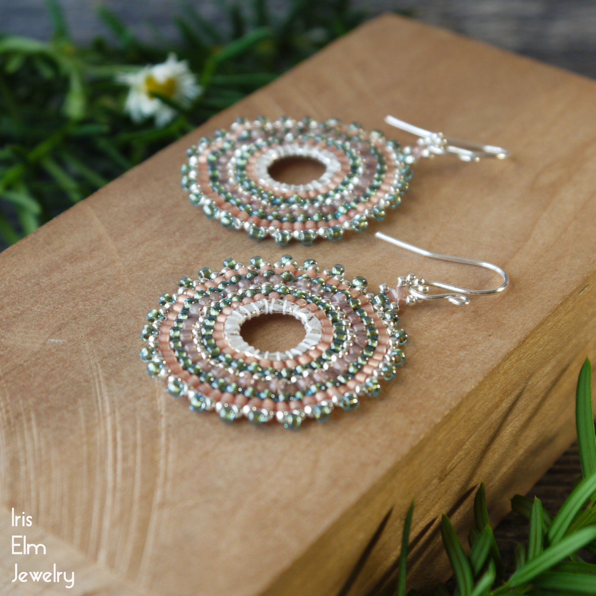 a pair of handmade woven hoop earrings with aqua, peach, and silver glass seed beads woven around metal link.