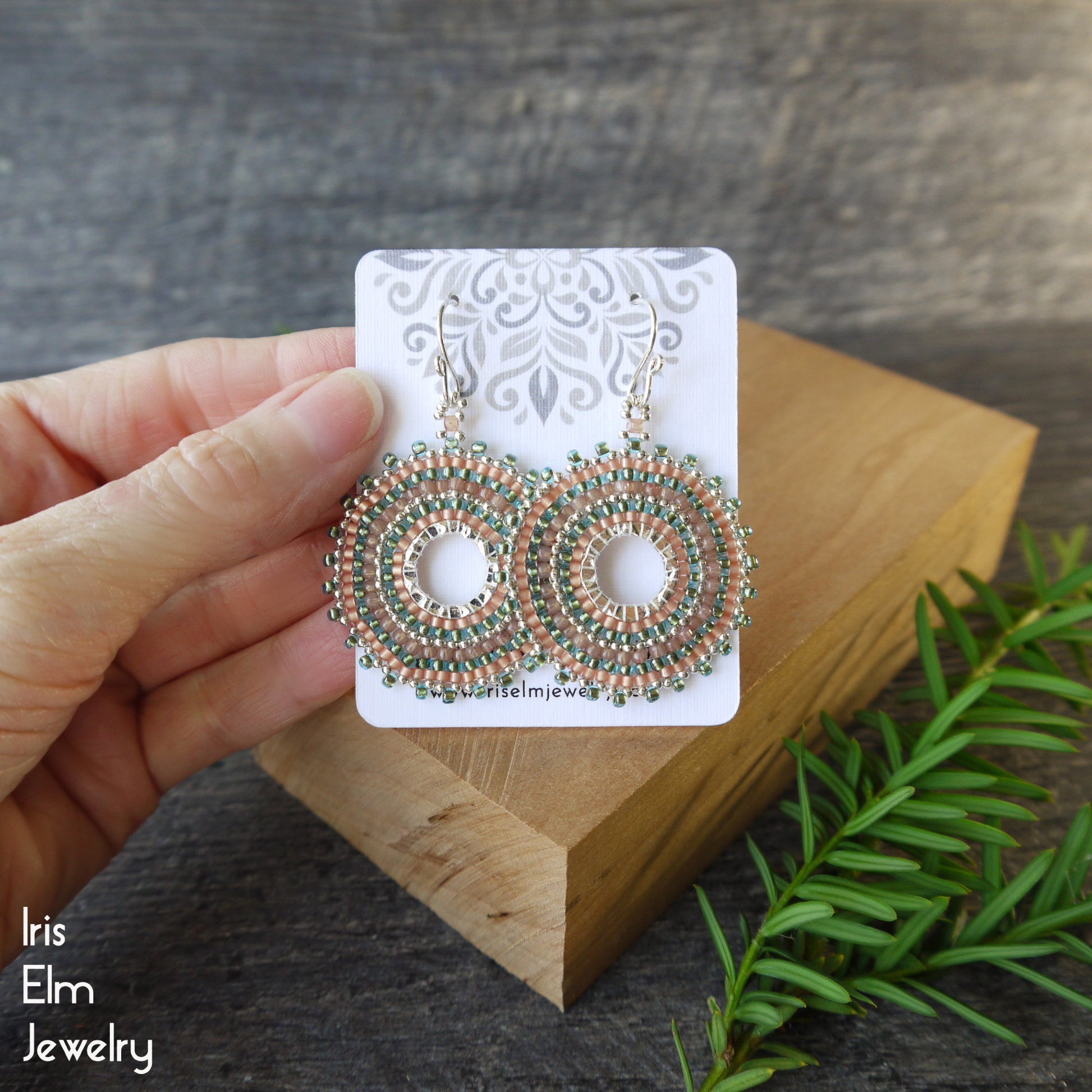 Decorative woven hoop aqua and peach seed bead earrings on a card held by a hand with a natural background