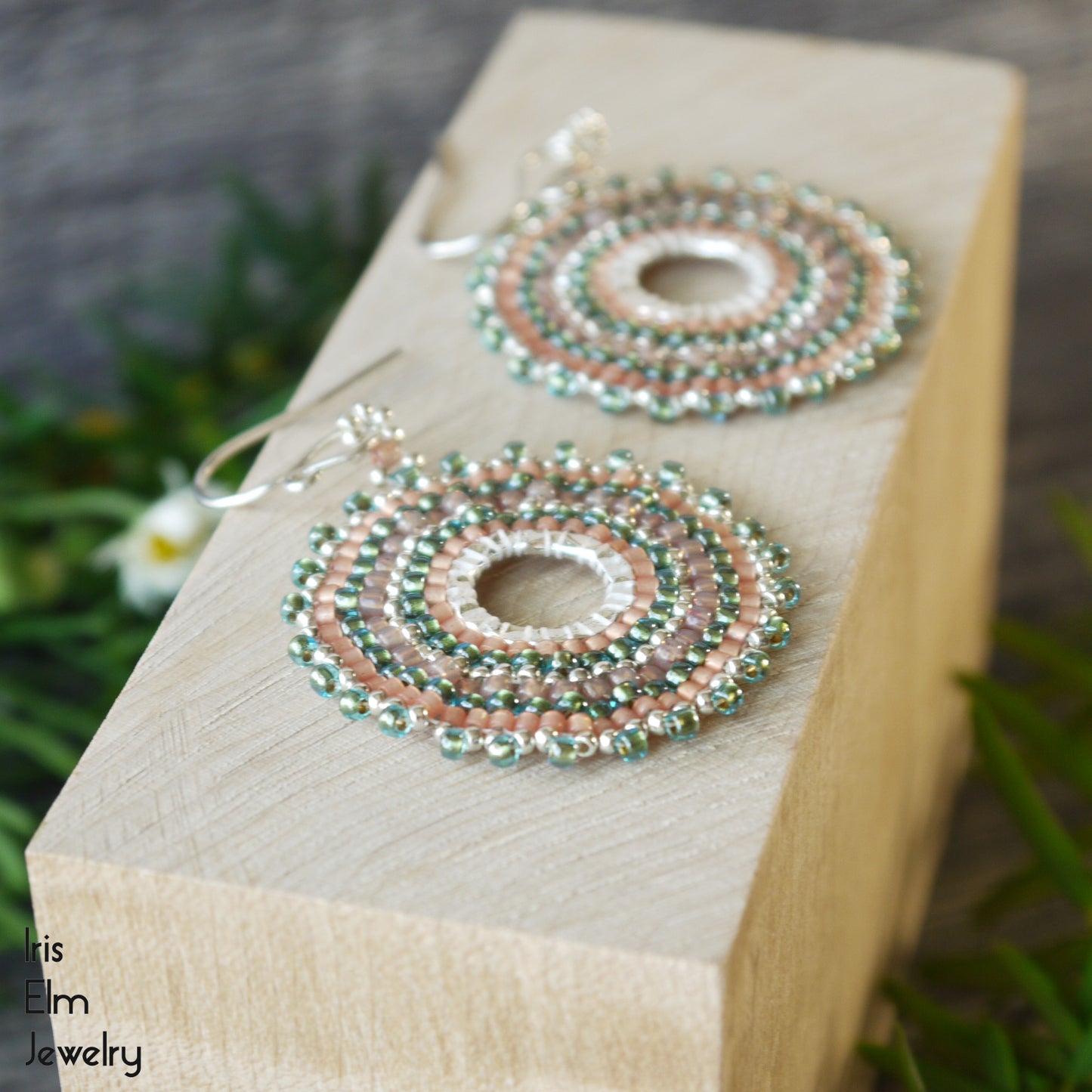 Circular beaded aqua and peach earrings with sterling silver ear wires on a wooden block with 'Iris Elm Jewelry' branding.