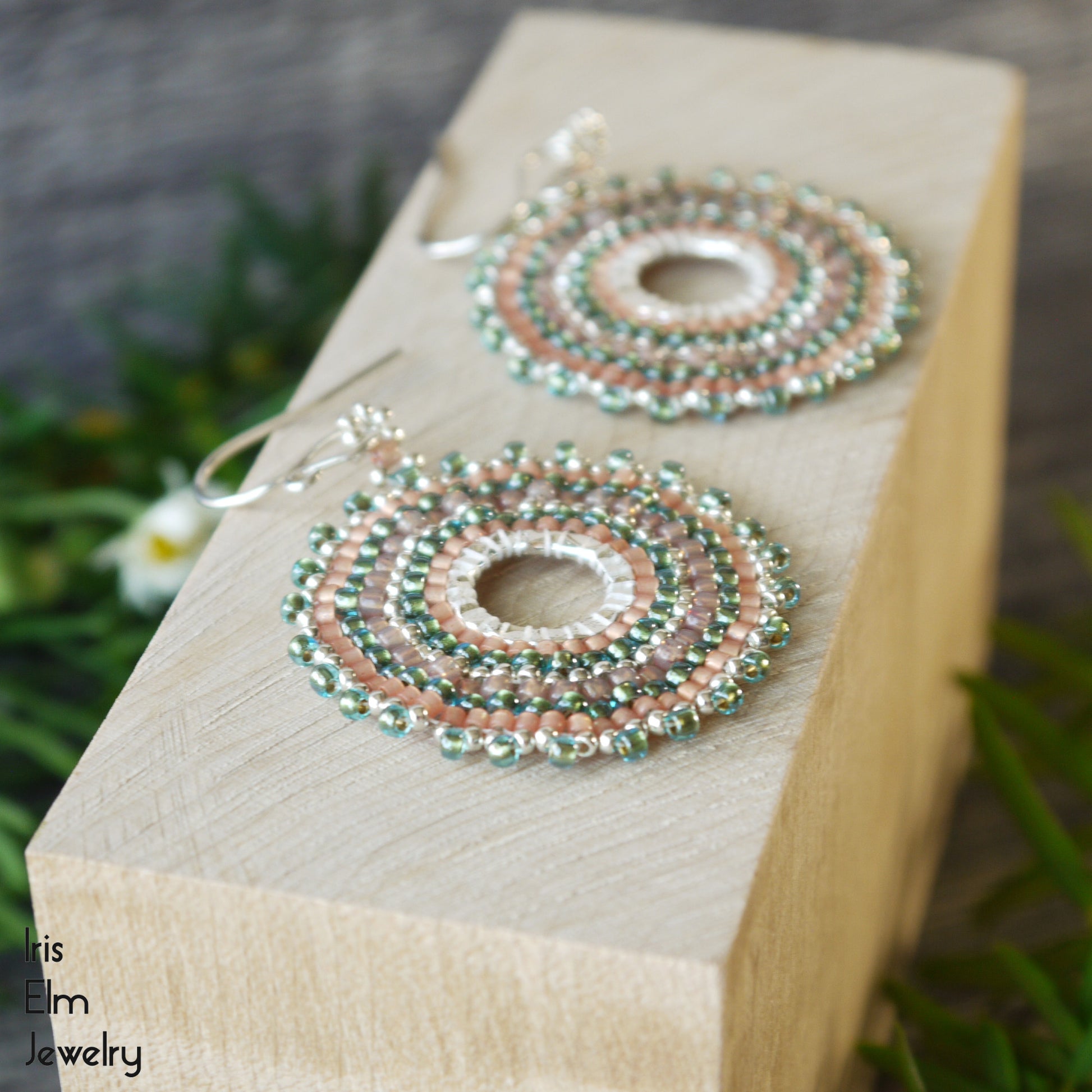 Circular beaded aqua and peach earrings with sterling silver ear wires on a wooden block with 'Iris Elm Jewelry' branding.