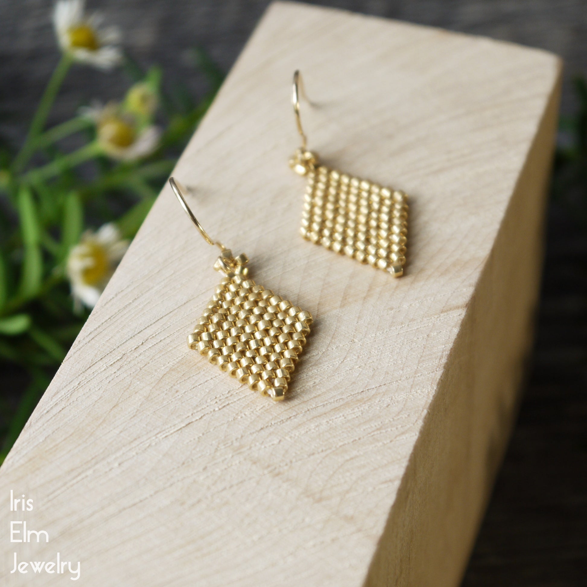 Gold beaded diamond shape small glass earrings on a wooden block with a natural background