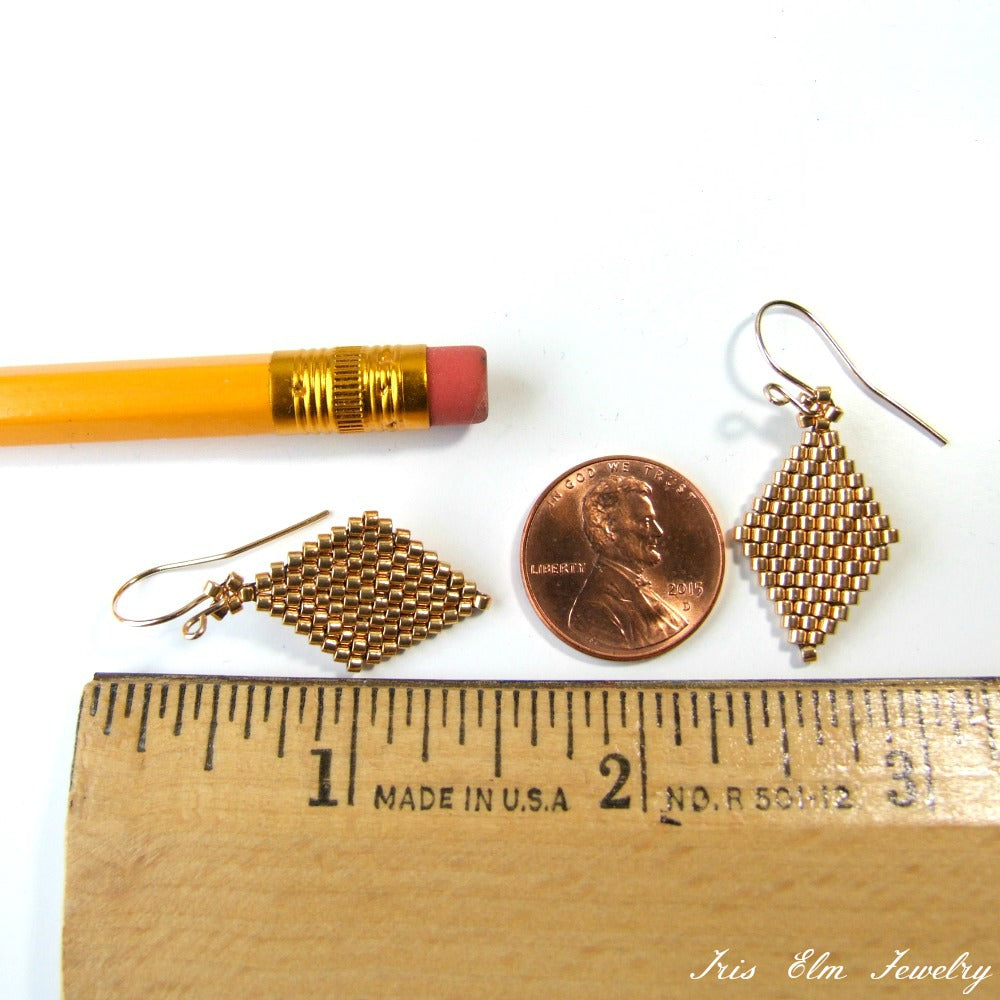 Gold earrings next to a penny and ruler for scale on a white background