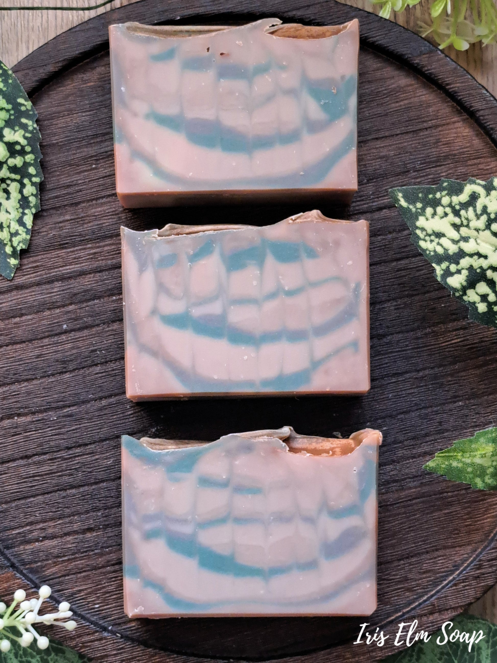 Three bars of Minnesota north woods handmade soap with a marbled design on a wooden surface, branded 'Iris Elfin Soap'.