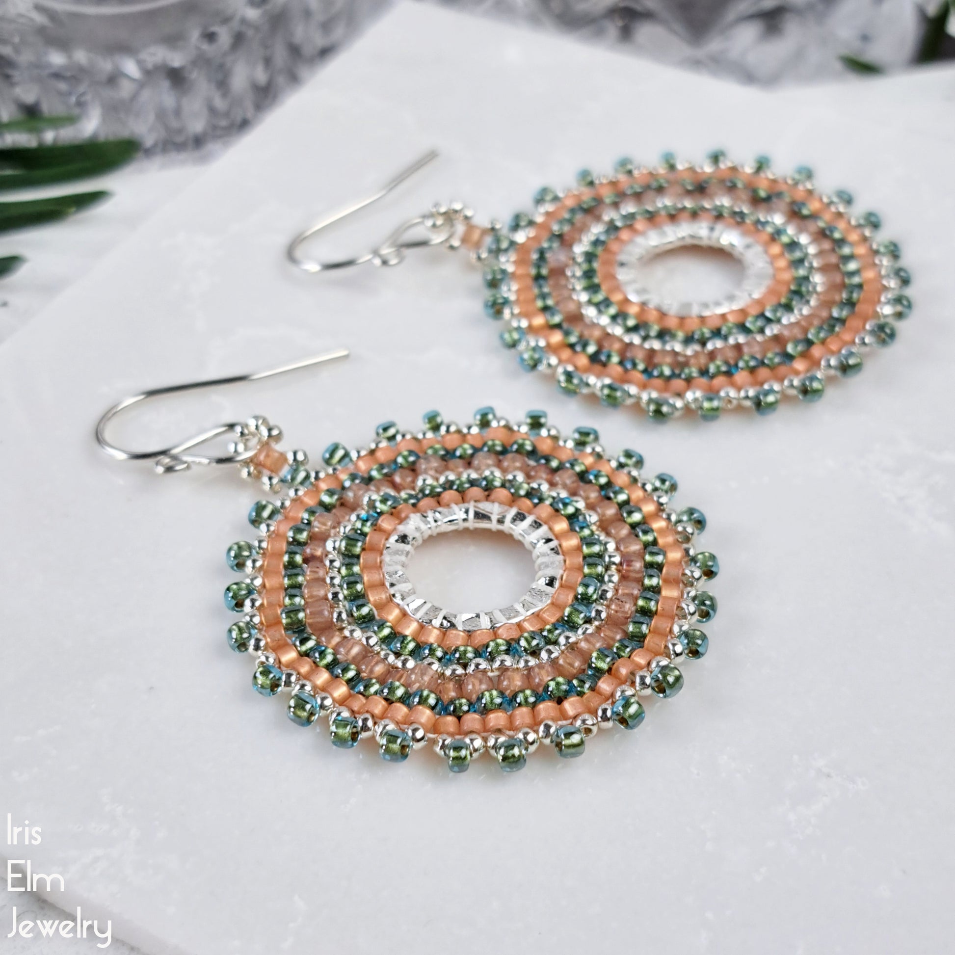 Beaded aqua and peach seed bead hoop earrings on a white surface with 'Iris Elm Jewelry' branding.