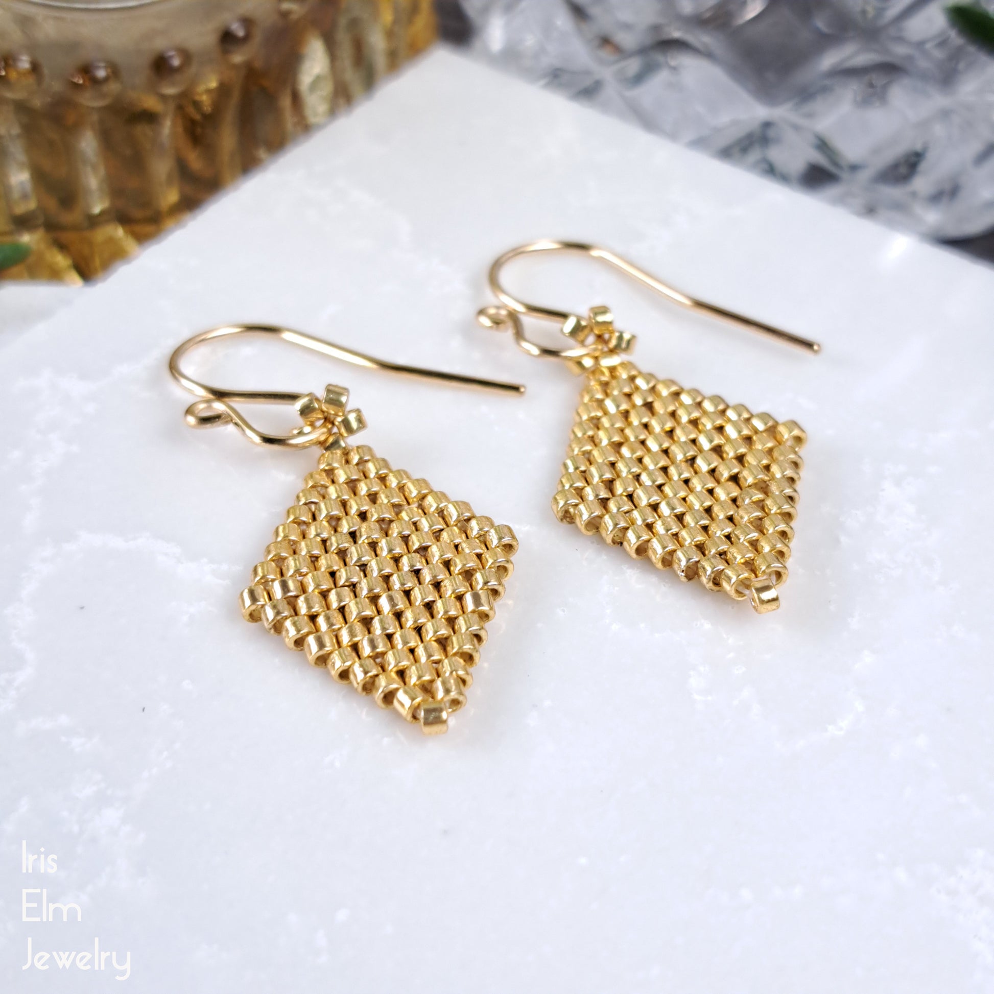 Gold seed bead beadwoven earrings on a white surface with 'The Elm Jewelry' branding.