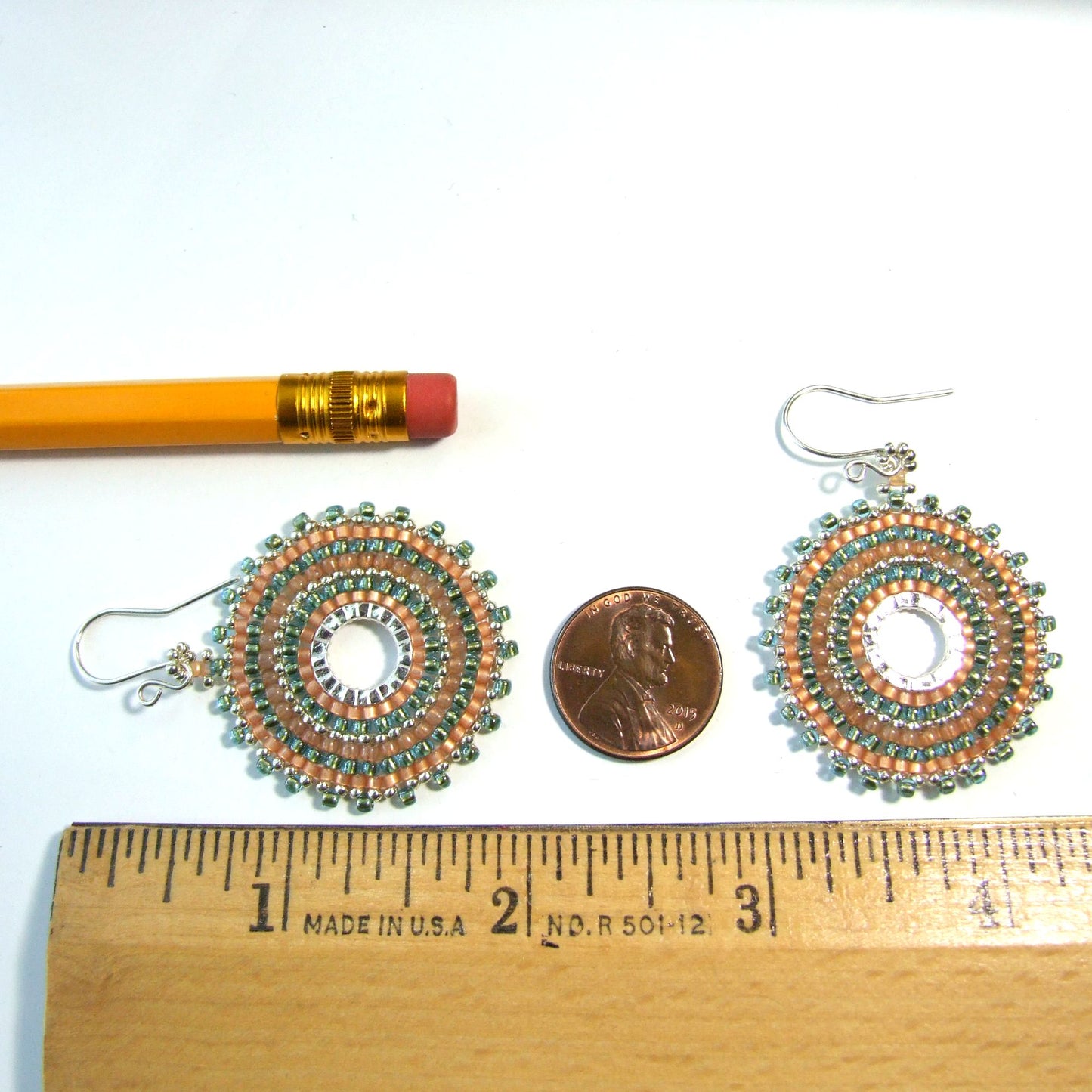 2-inch-long Pair of beaded hoop earrings next to a pencil and penny for scale, with a ruler at the bottom.