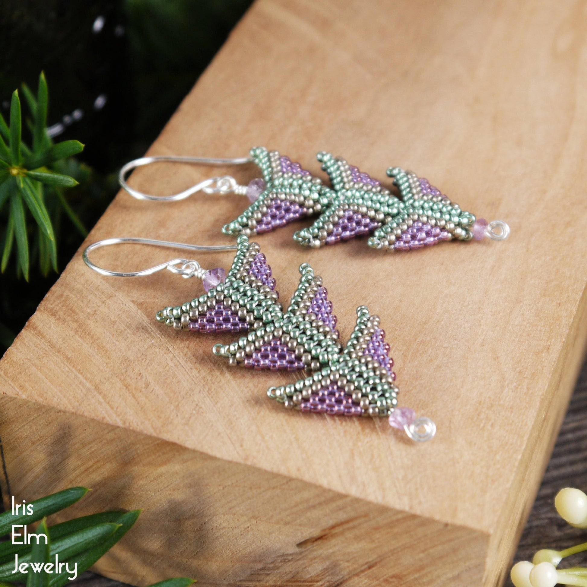 Beaded purple and green three-tiered triangle seed bead earrings with amethyst on a wooden block with 'Iris Elm Jewelry' branding.