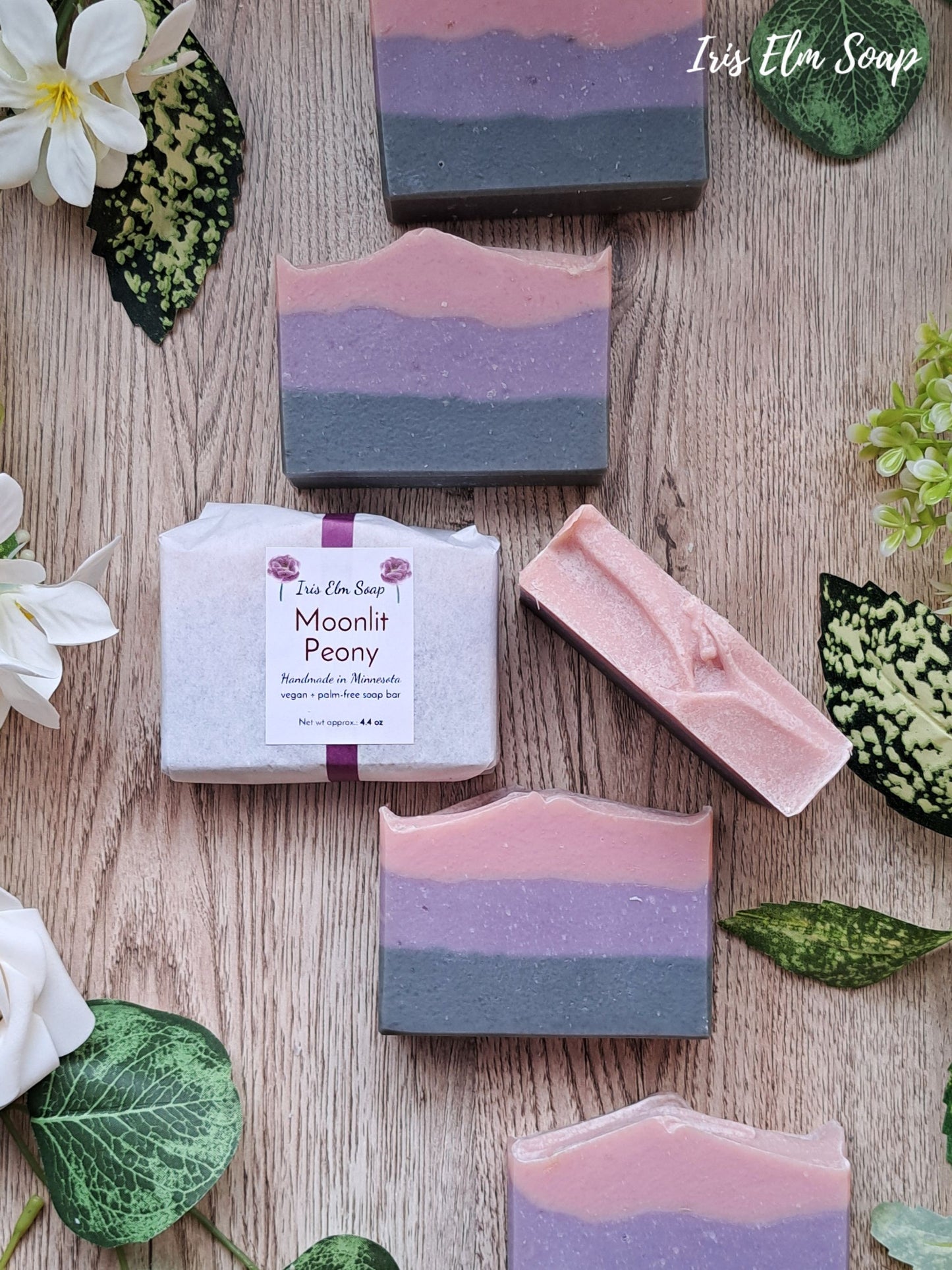 Iris Elm Soap bars with 'Moonlit Peony' packaging on a wooden surface with flowers and leaves.