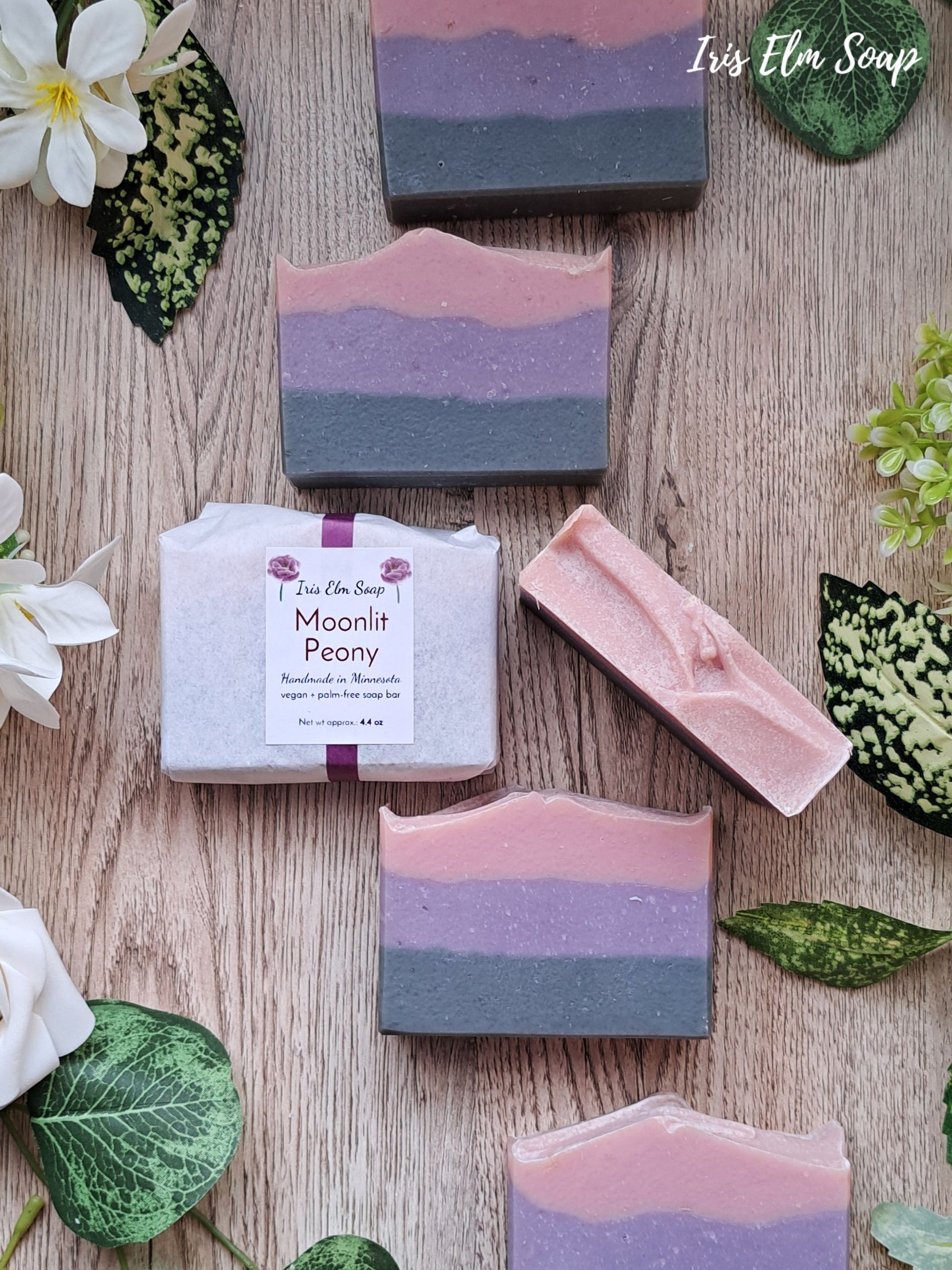 Iris Elm Soap bars with 'Moonlit Peony' packaging on a wooden surface with flowers and leaves.