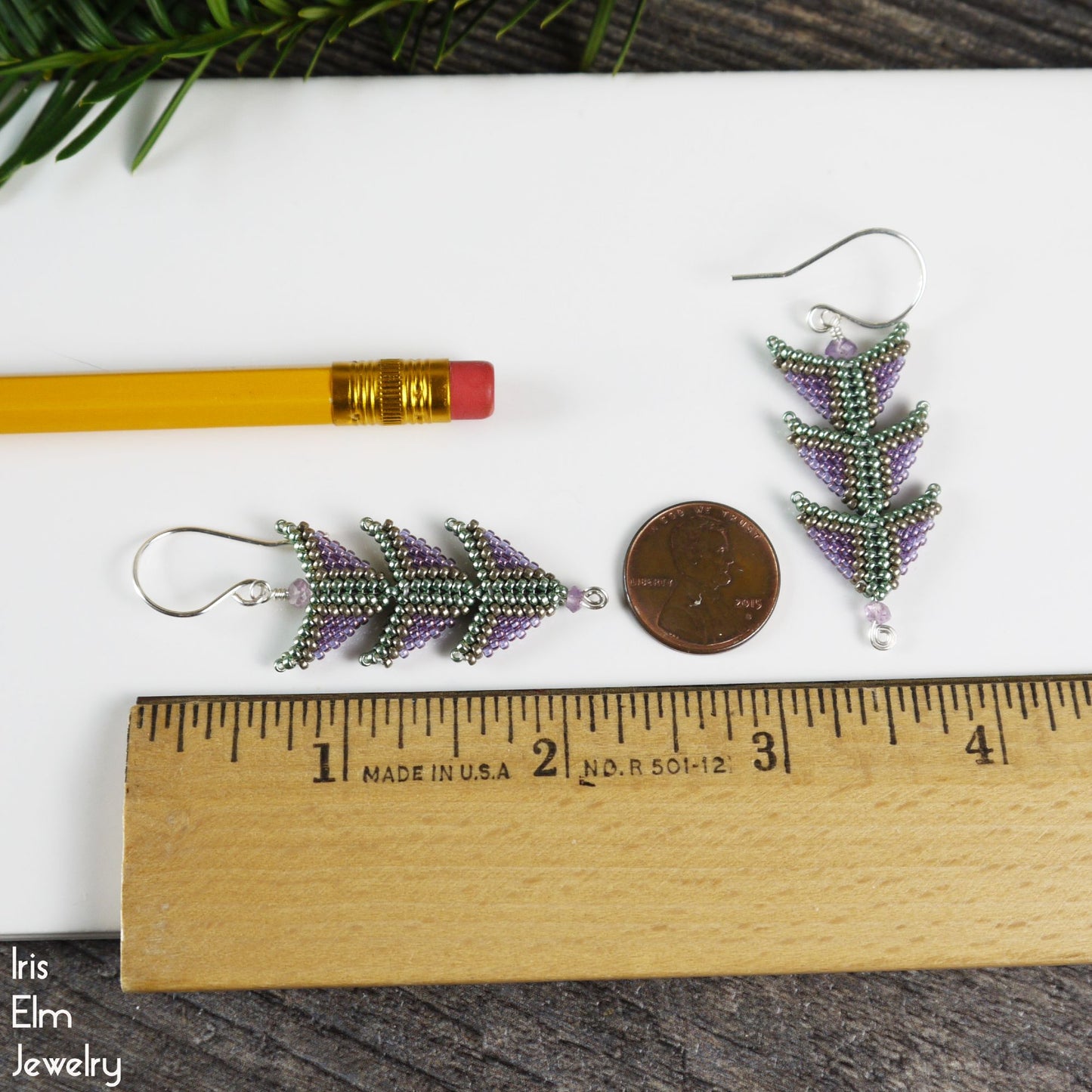 Beaded 2.25 inch long triangle tiered earrings next to a ruler for scale on a white surface with a pencil and coin.