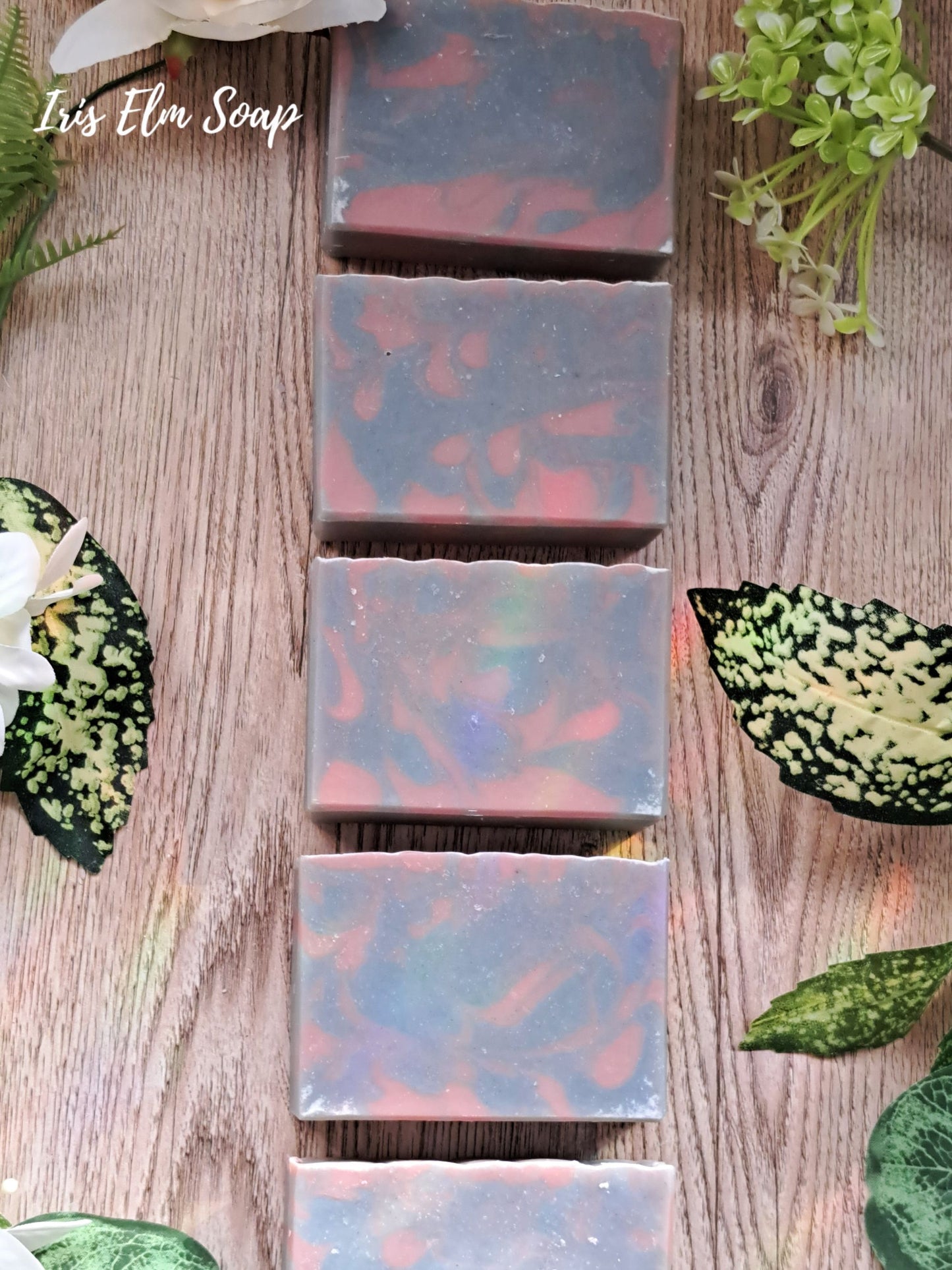 Iris Elm Soap bars with marbled design on a wooden surface with green leaves.