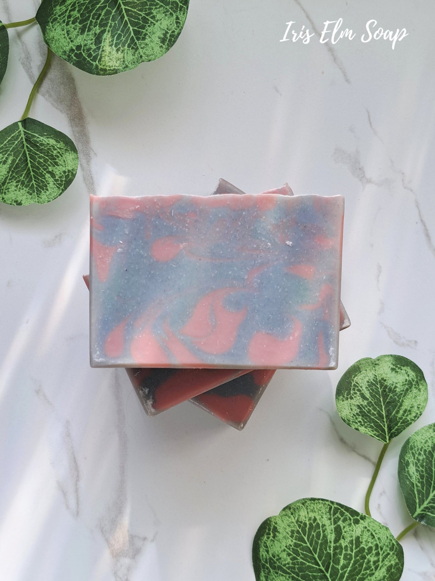 Marbled lavender handmade soap bar on a white surface with green leaves