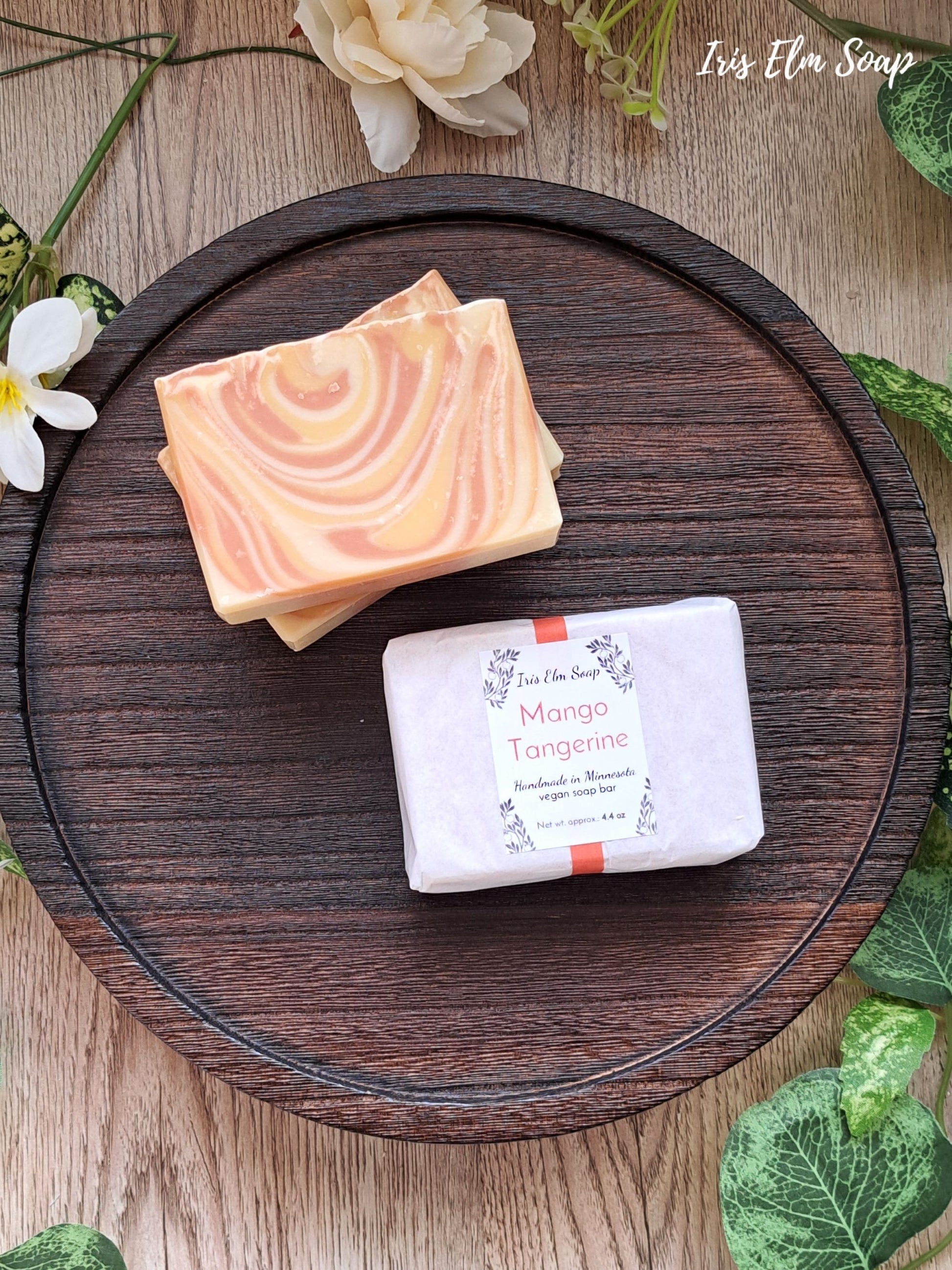 Two mango tangerine handmade soap bars on a wooden tray with greenery around
