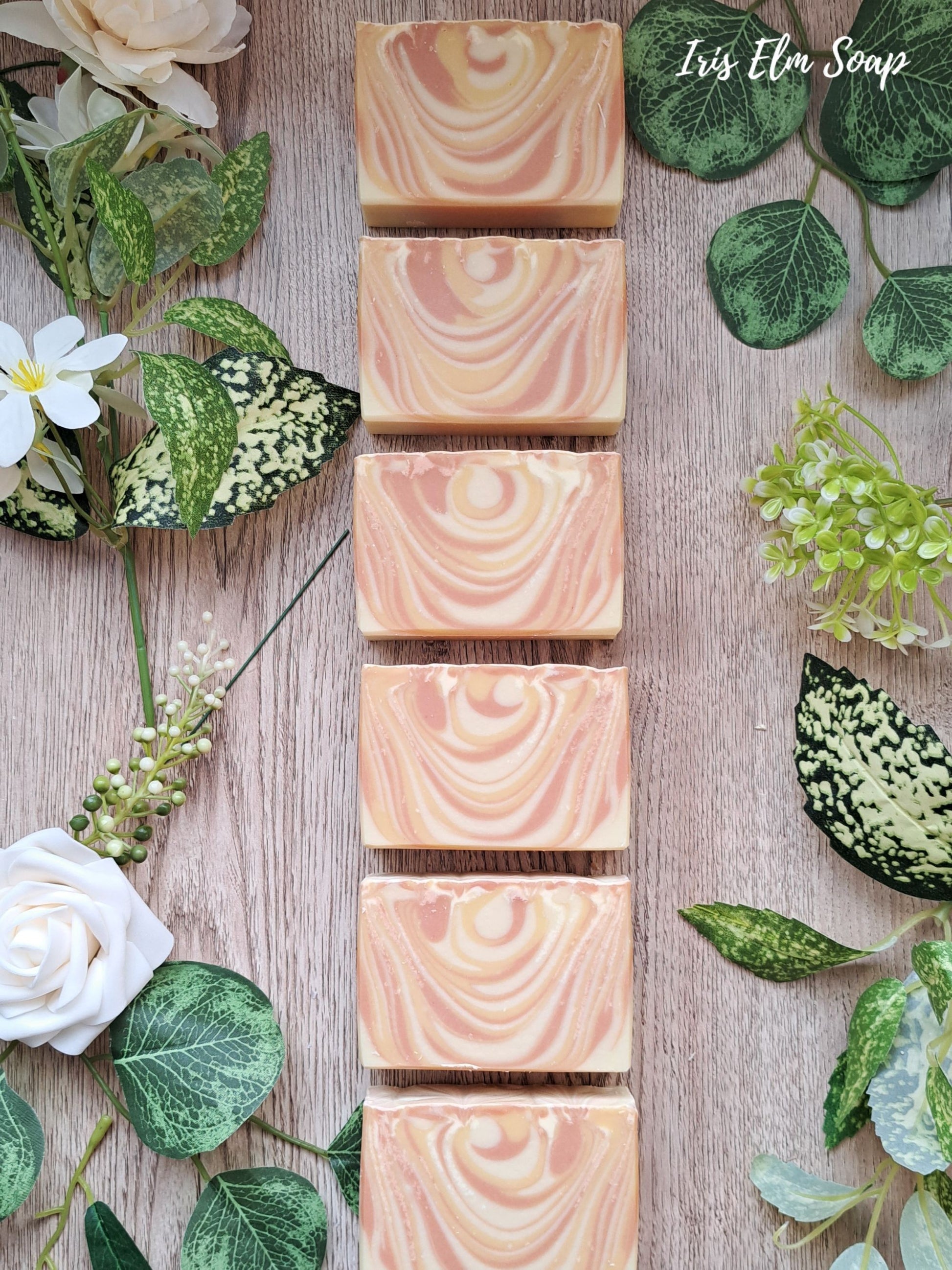 Row of mango tangerine handmade soap bars on a wooden surface with green leaves and flowers