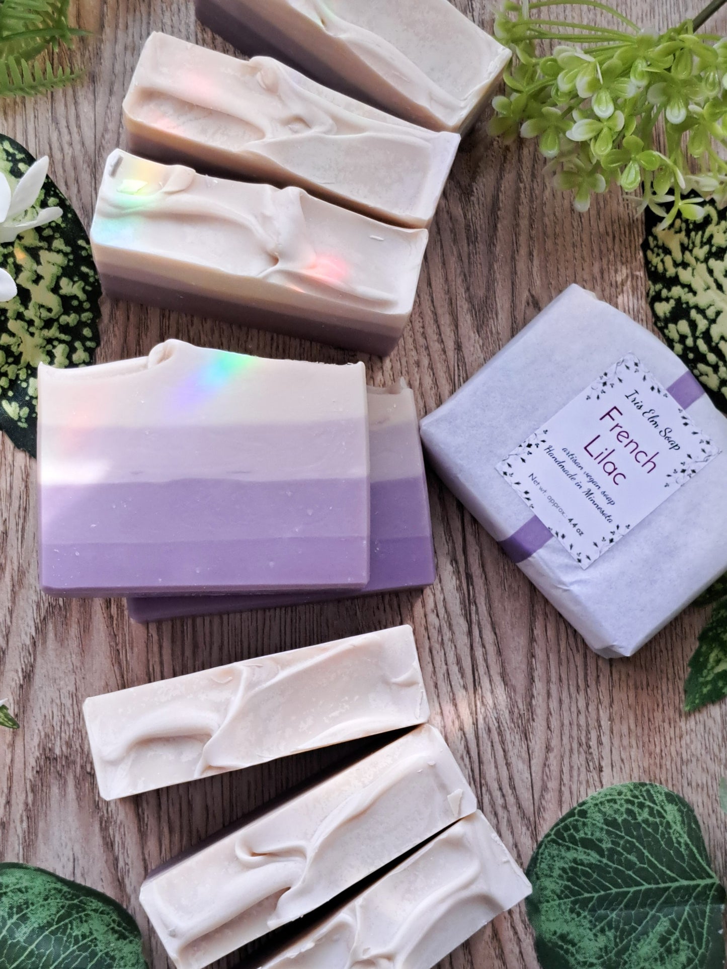 French lilac Handmade soap bars with a gradient of colors on a wooden surface, surrounded by green leaves.