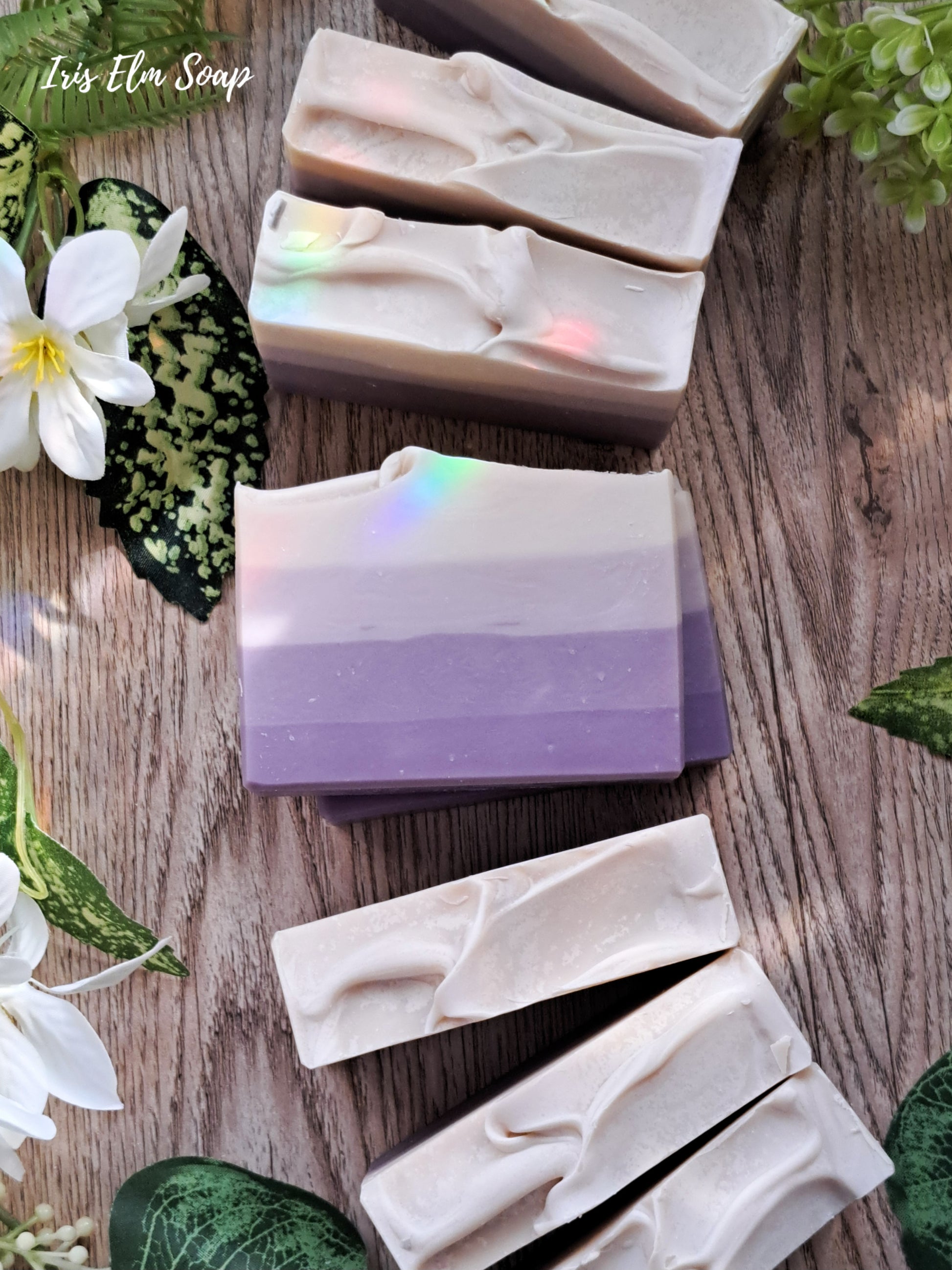 Handmade lilac flower scented soap bars with a purple gradient design on a wooden surface with greenery.