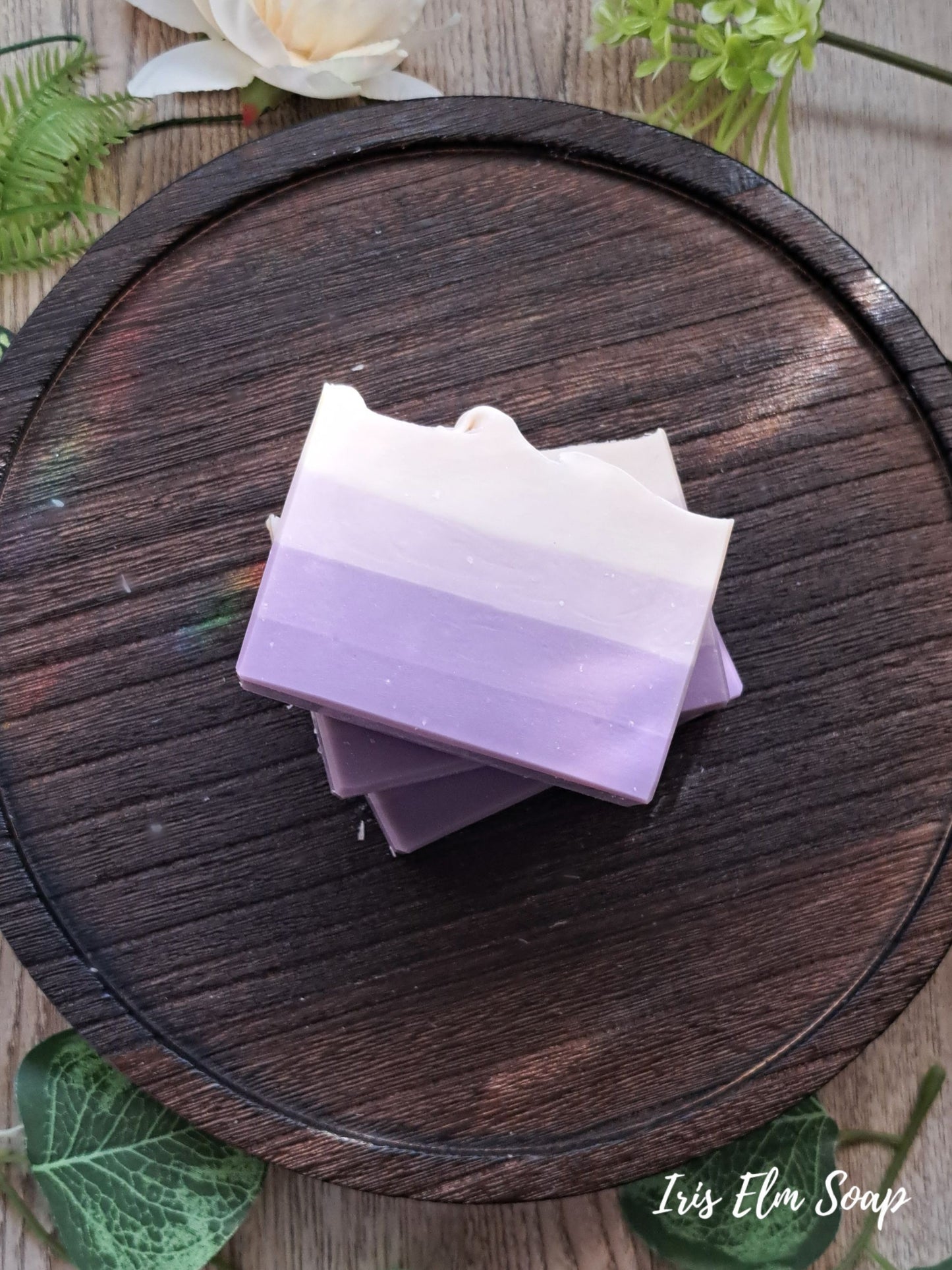 Stack of purple French lilac handmade vegan soap bars on a wooden surface with greenery around