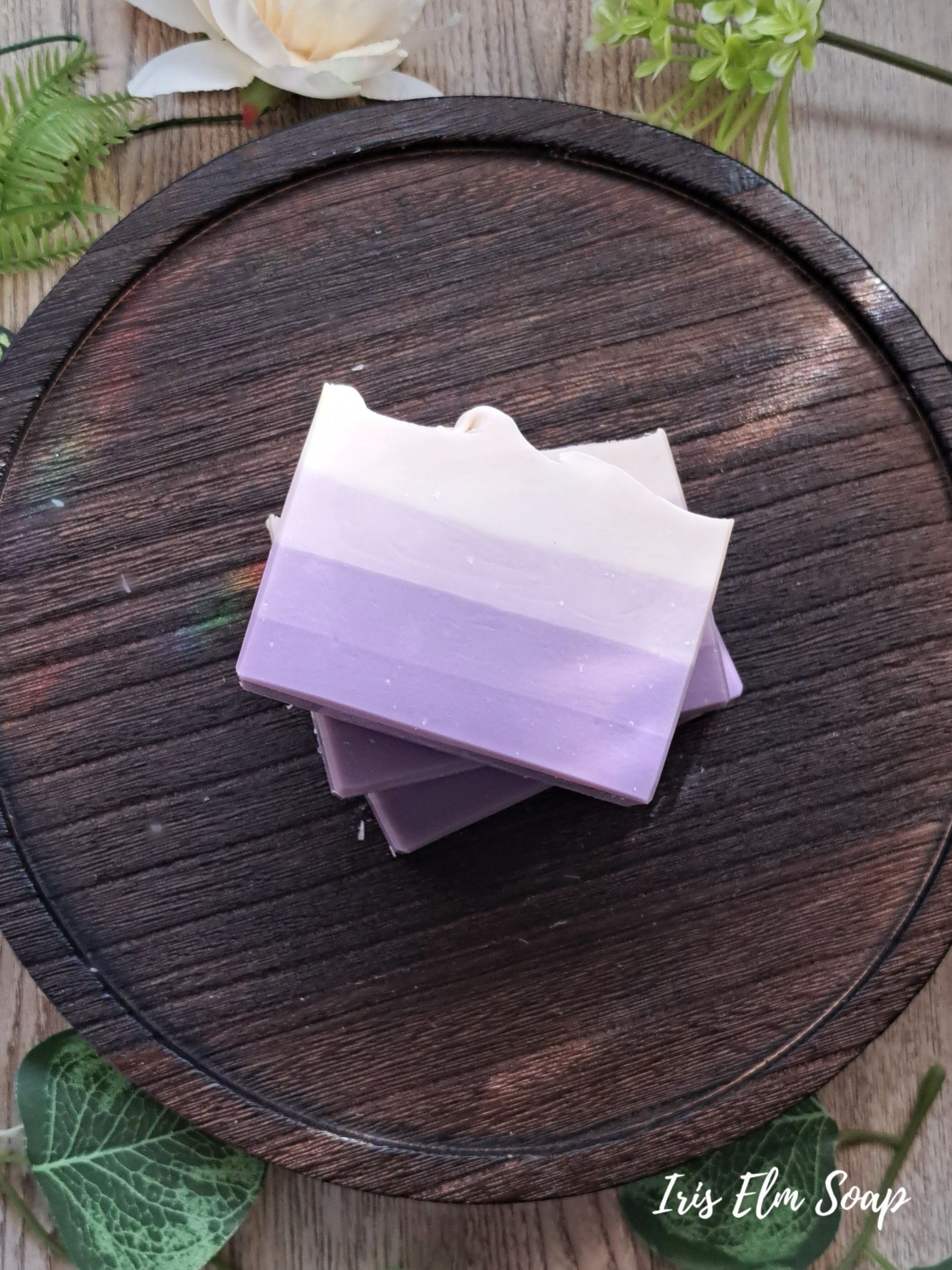 Stack of purple French lilac handmade vegan soap bars on a wooden surface with greenery around