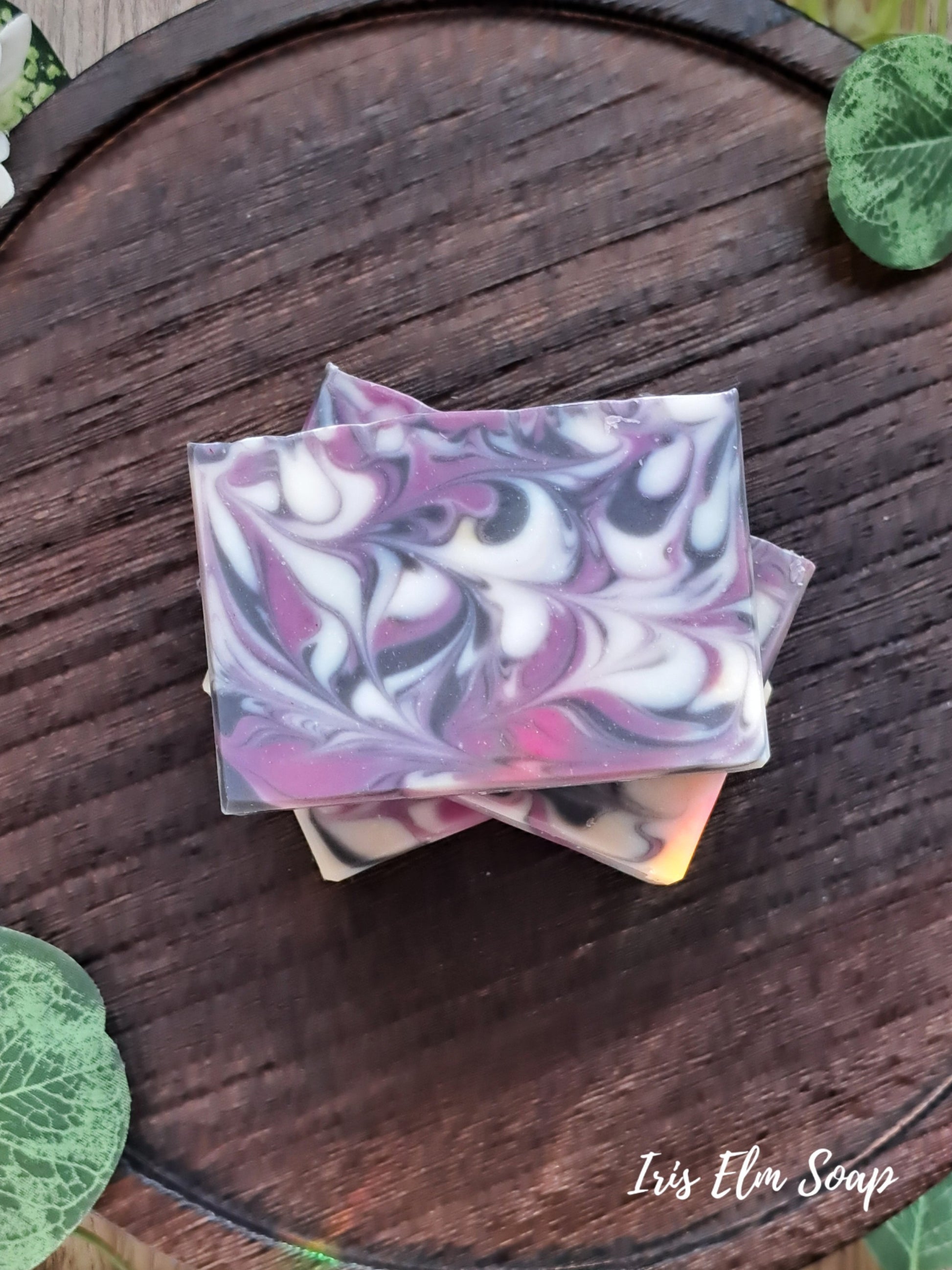 Stack of marbled soap black raspberry vanilla handmade bars on a wooden surface with 'Iris Elm Soap' branding.