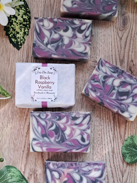 Marbled purple and white soap bars on a wooden surface with a label for 'Black Raspberry Vanilla'.