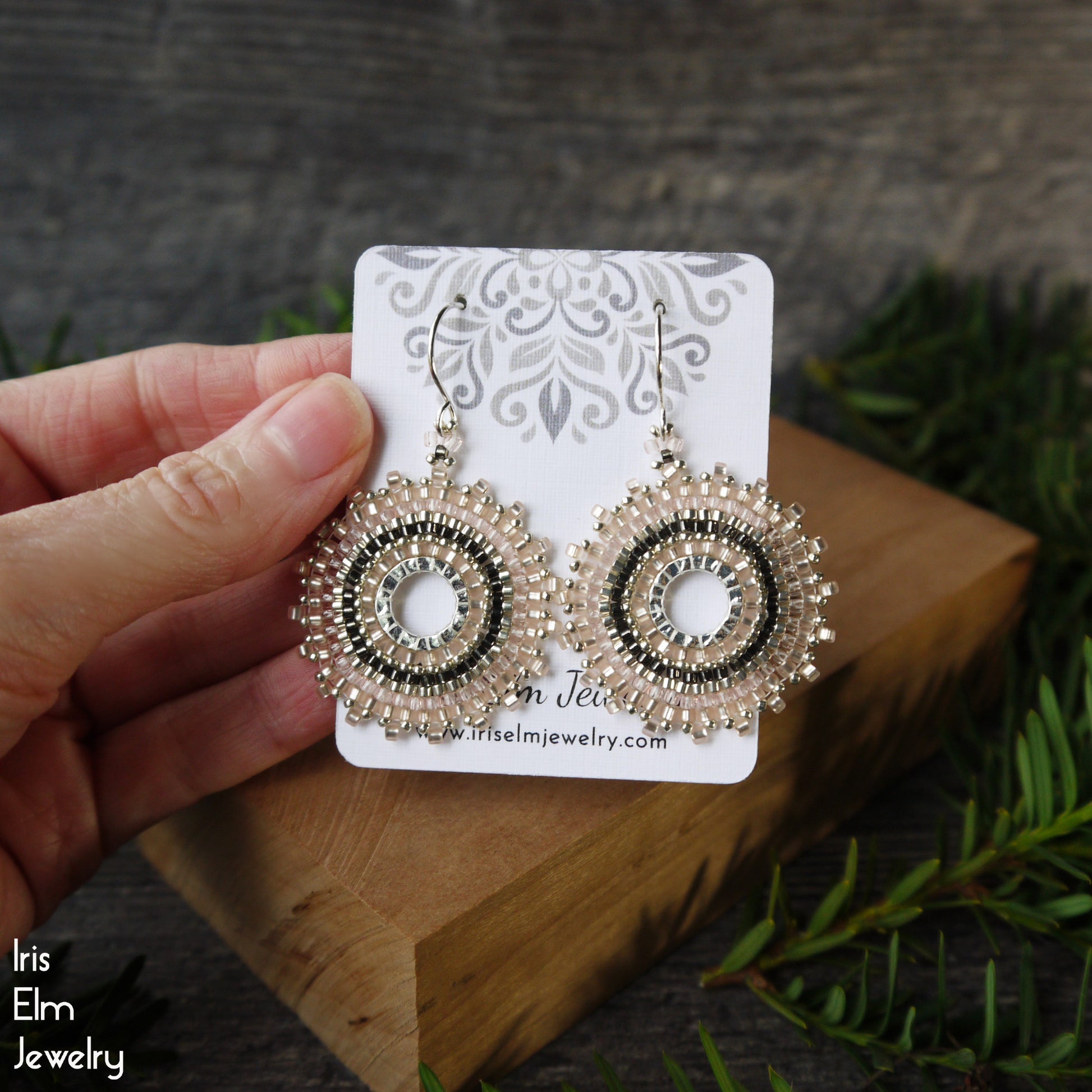 Decorative pink hoop earrings on a card held by a hand with a natural background