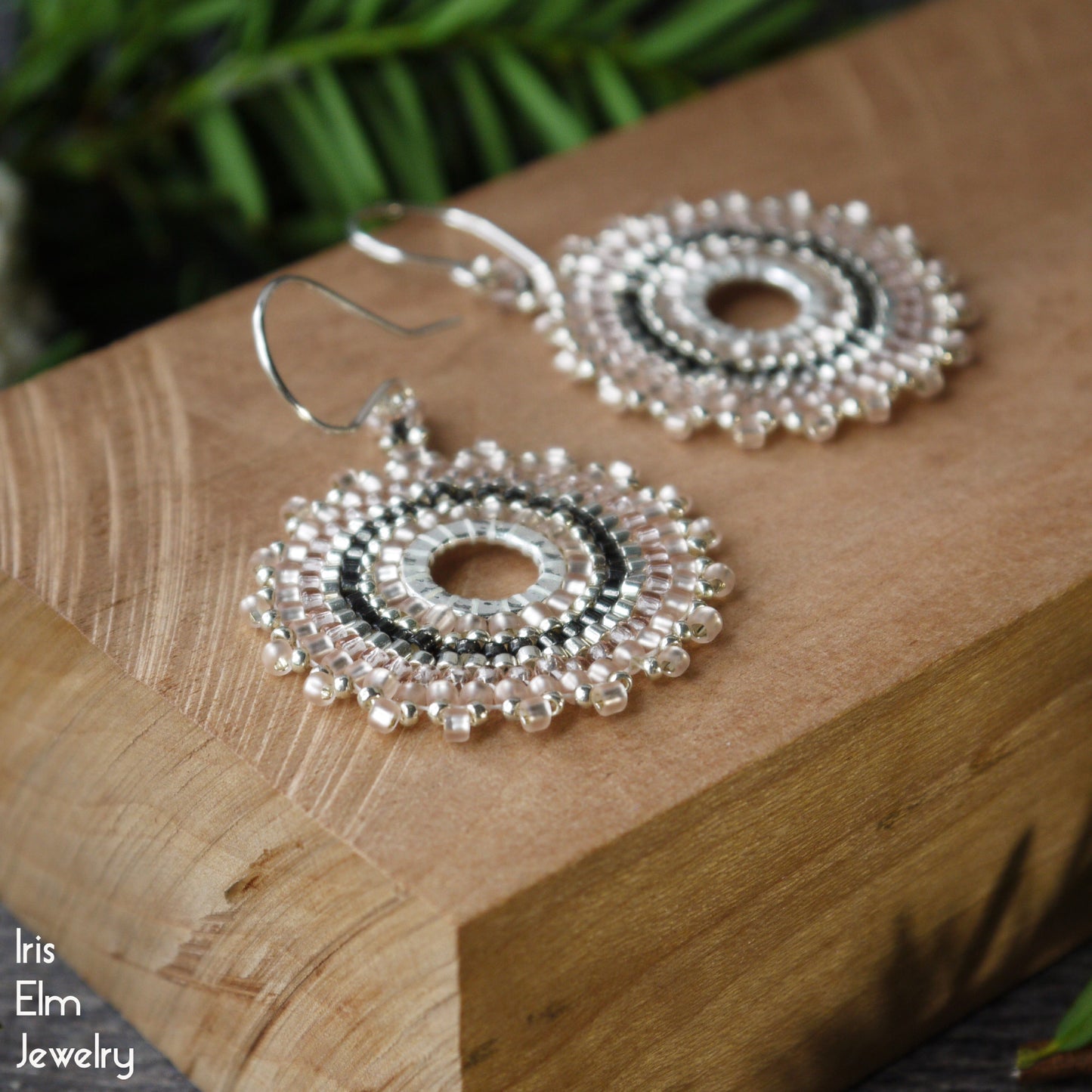 Decorative pale pink glass seed bead circular hoop earrings on a wooden surface with 'Iris Elm Jewelry' branding.