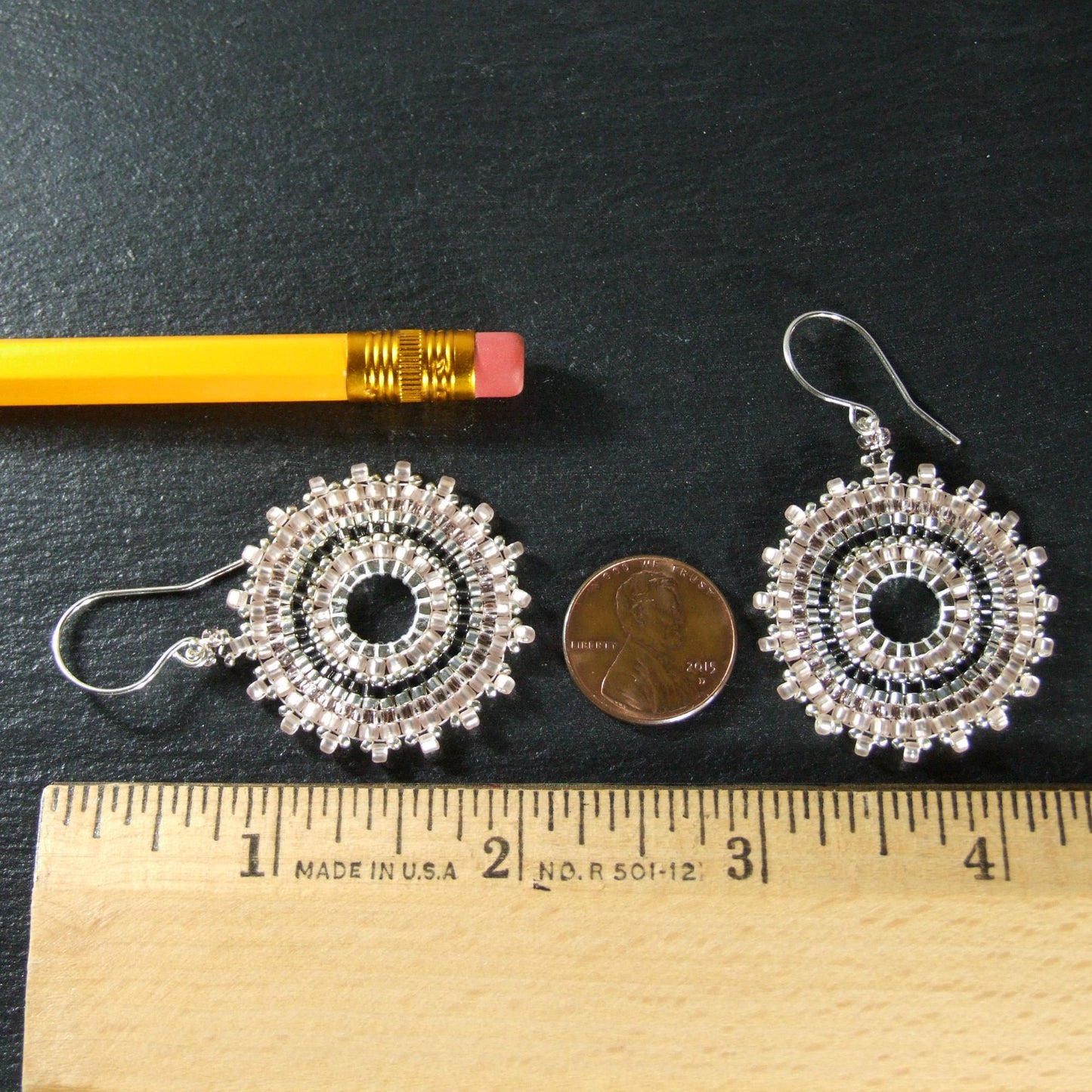 2-inch-long pink seed bead hoop earrings alongside a ruler, pencil, and penny for scale against black background