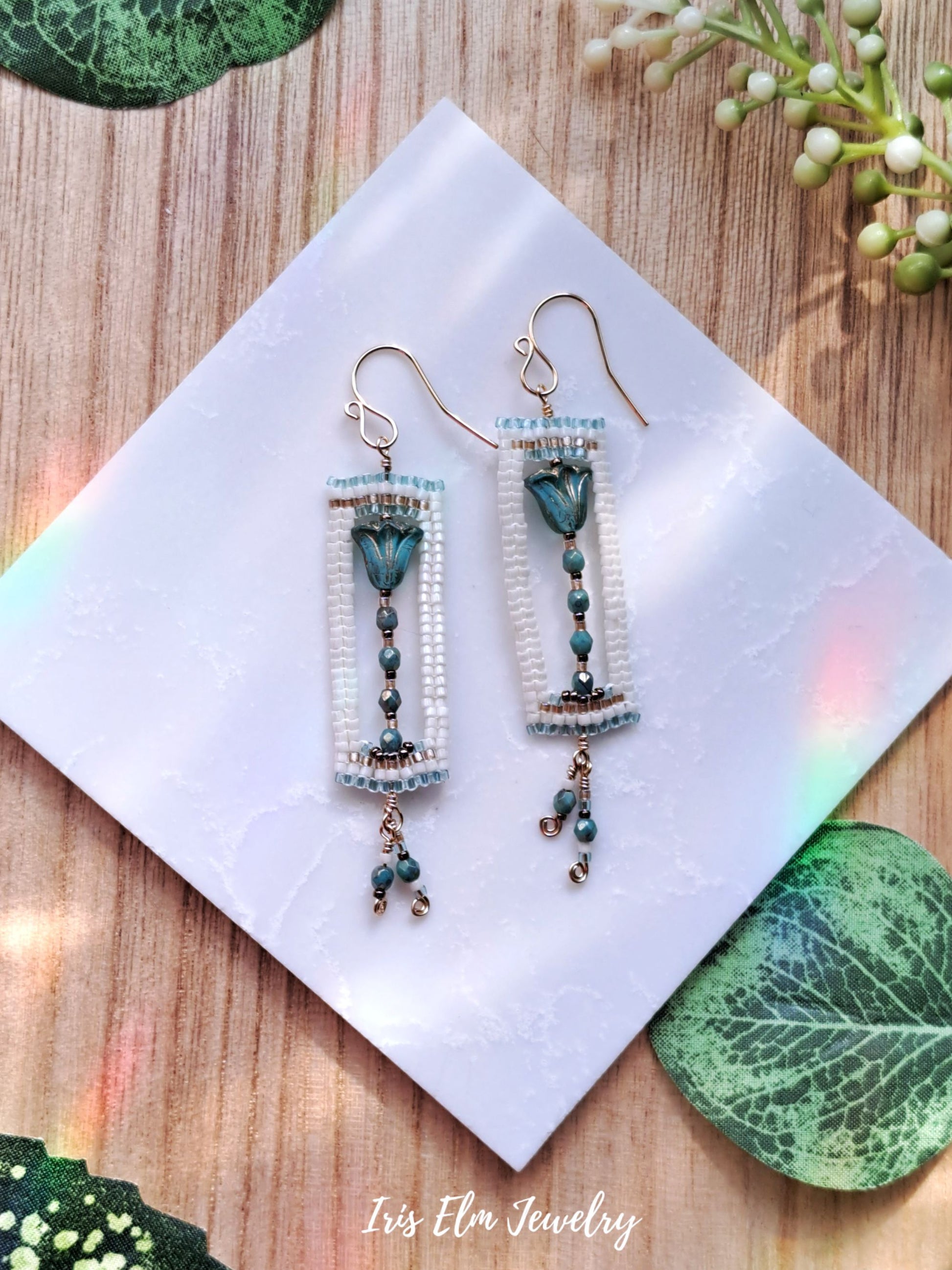 Pair of beaded tulip goldfilled earrings on a white tile with green leaves in the background