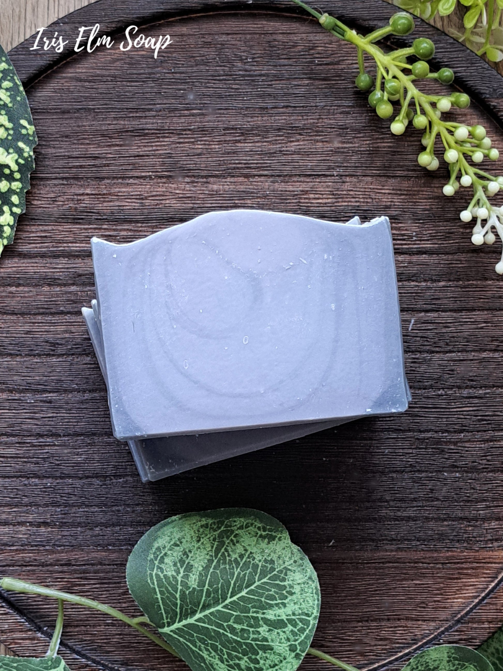Two bars of cedar musk and lavender handmade soap stacked on a wooden surface with greenery around