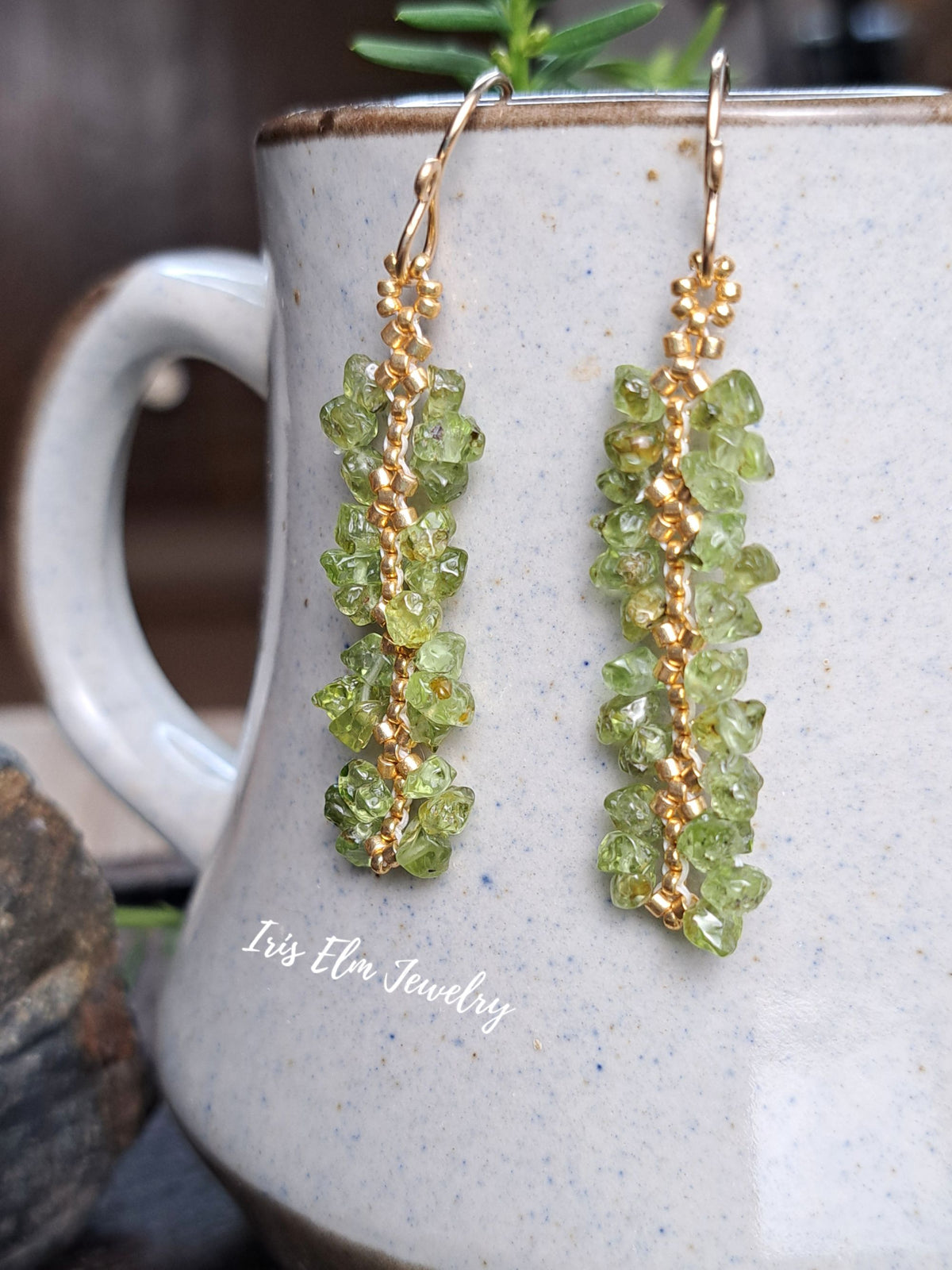 beaded green peridot chip with gold seed bead earrings by Iris Elm Jewelry dangling from ceramic pottery