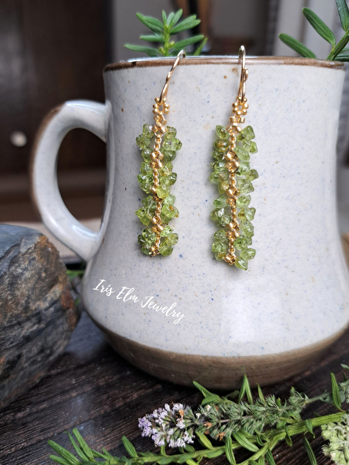 beaded green peridot chip with gold seed bead earrings by Iris Elm Jewelry dangling from ceramic pottery