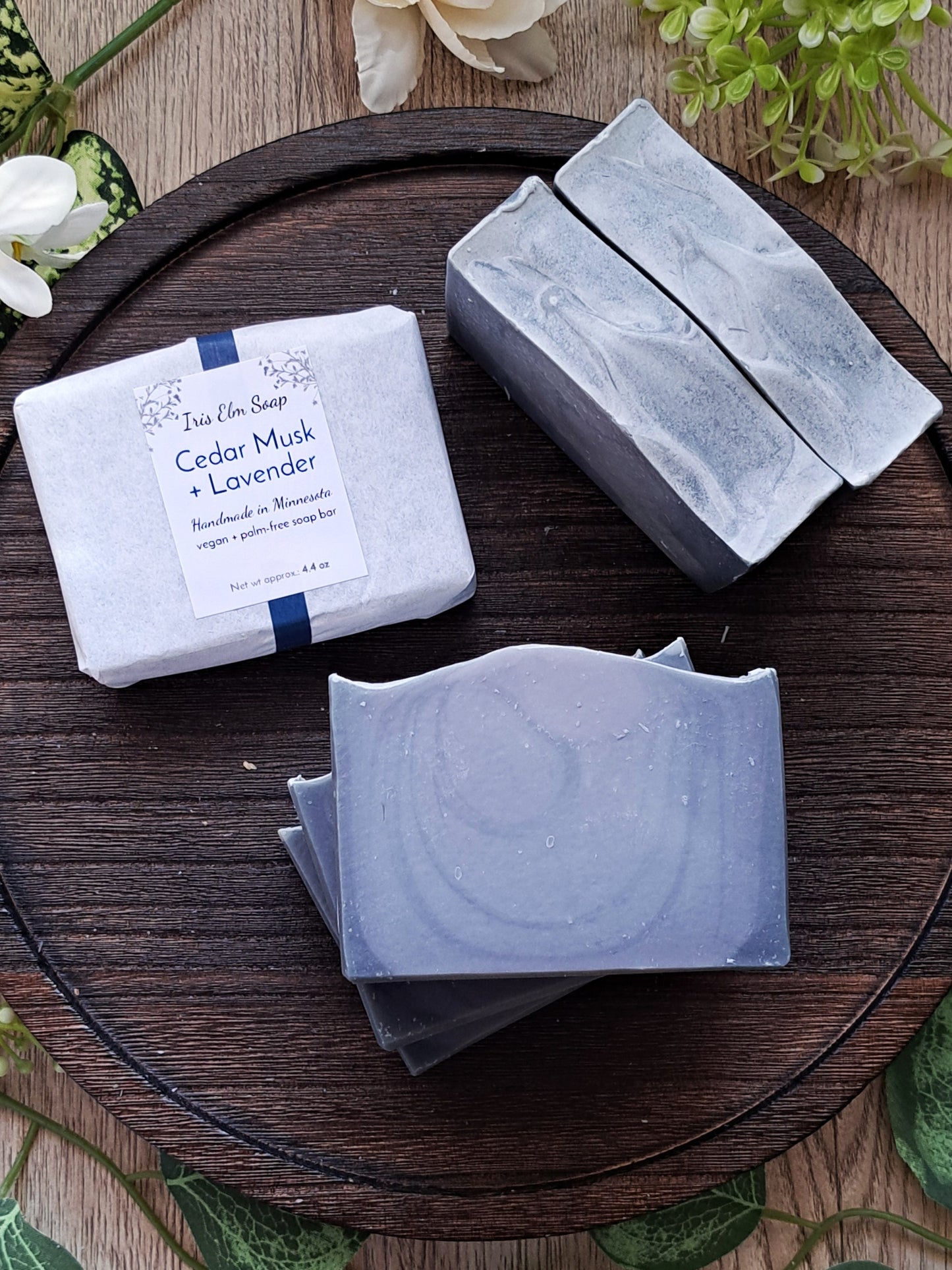 Three bars of handmade Iris Elm soap on a wooden surface with a label indicating 'Cedar Musk + Lavender'.