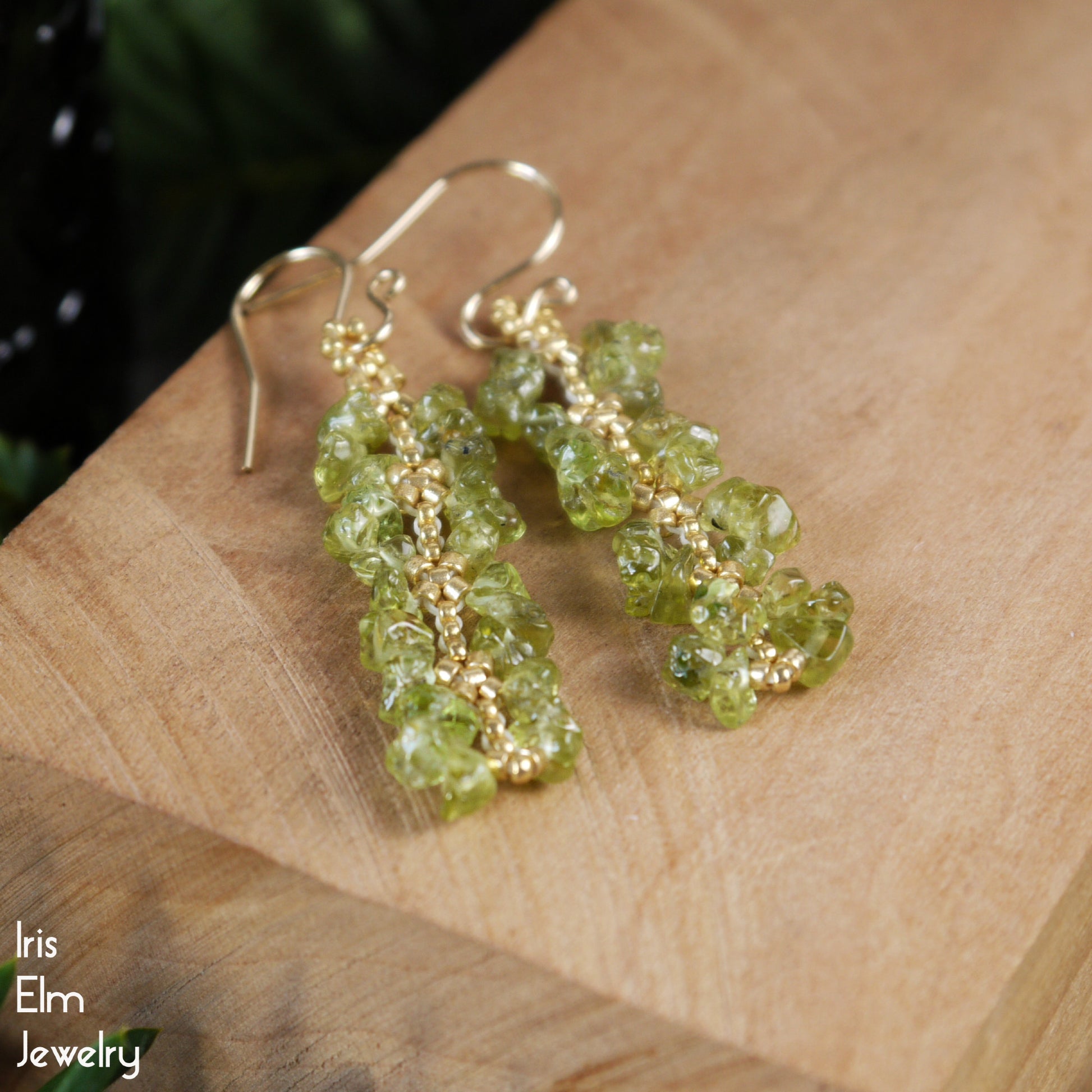 Green gemstone earrings on a wooden surface with 'Iris Elm Jewelry' branding.