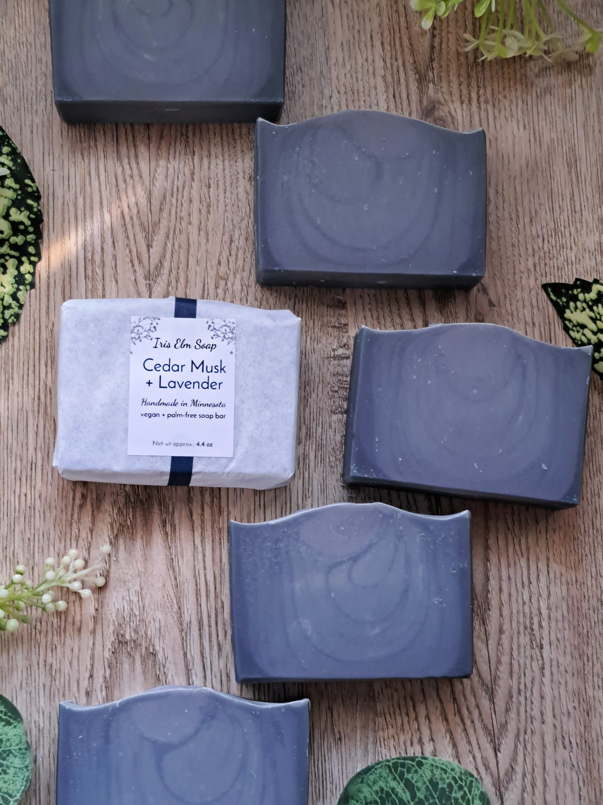 Bar of cedar musk and lavender handmade soap with a label on a wooden surface surrounded by greenery