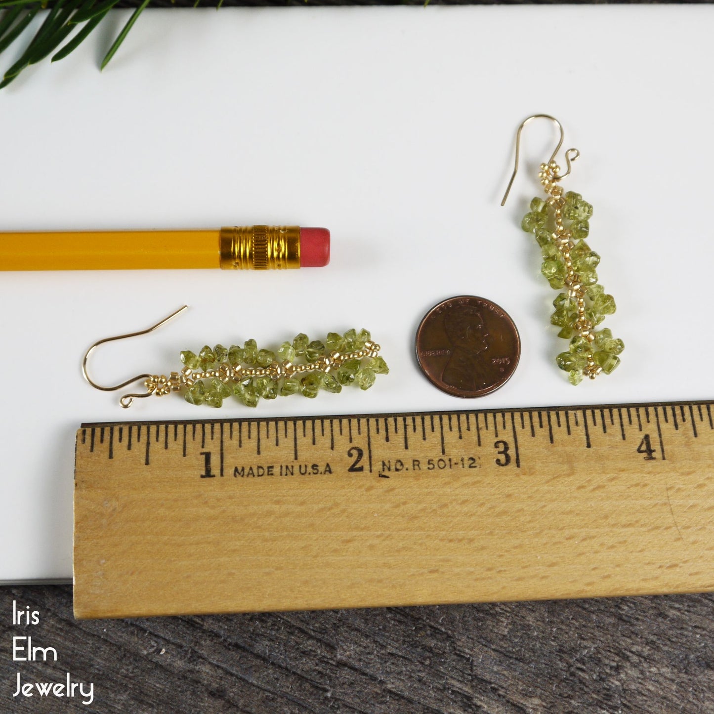 2 and 1/8 inch long Green beaded earrings with gold hooks on a ruler, pencil, and coin for scale on a white background.