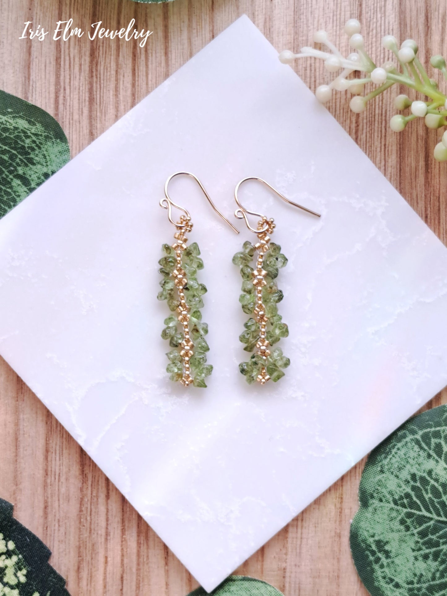 Green beaded peridot stone earrings on a white napkin with 'Iris Elm Jewelry' branding.