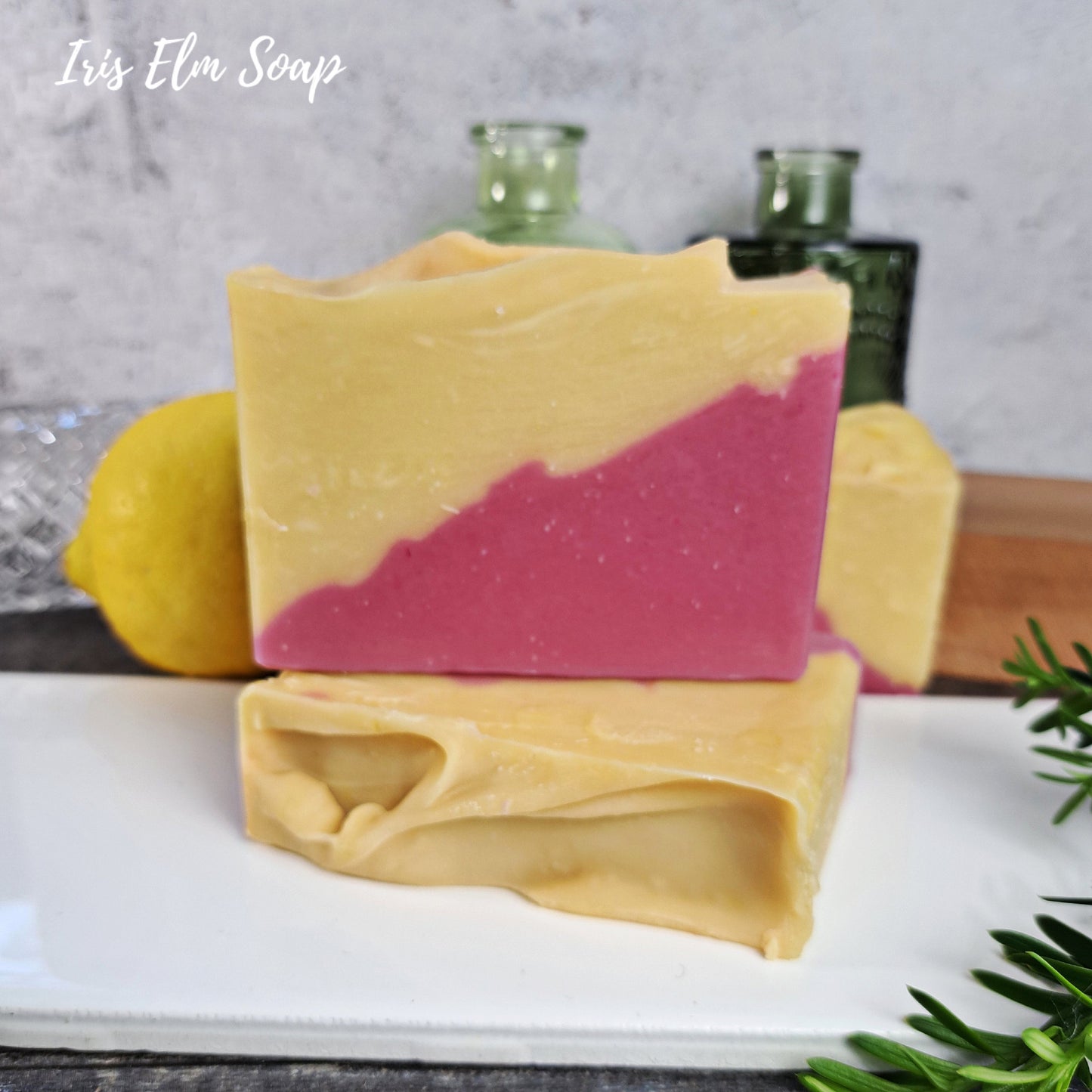 Two bars of cherry lemonade handmade soap with a pink and yellow coloration on a white surface, with 'Iris Elm Soap' branding.