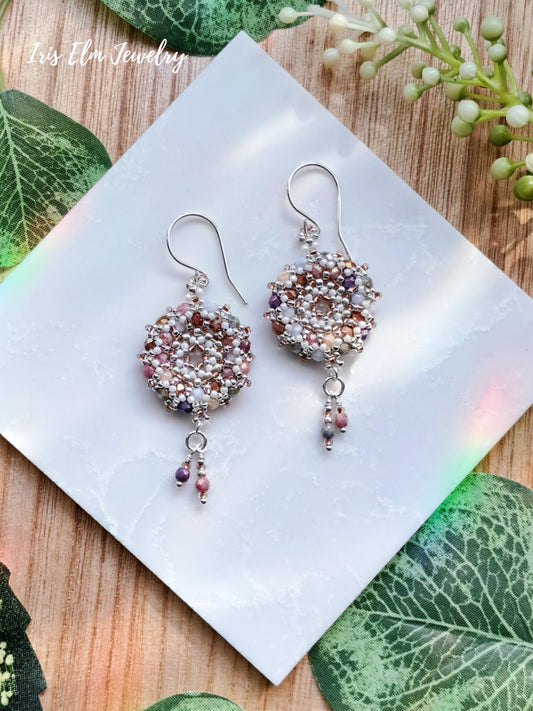 Pair of beaded multi color glass wreath hoop earrings on a white card with green leaves in the background