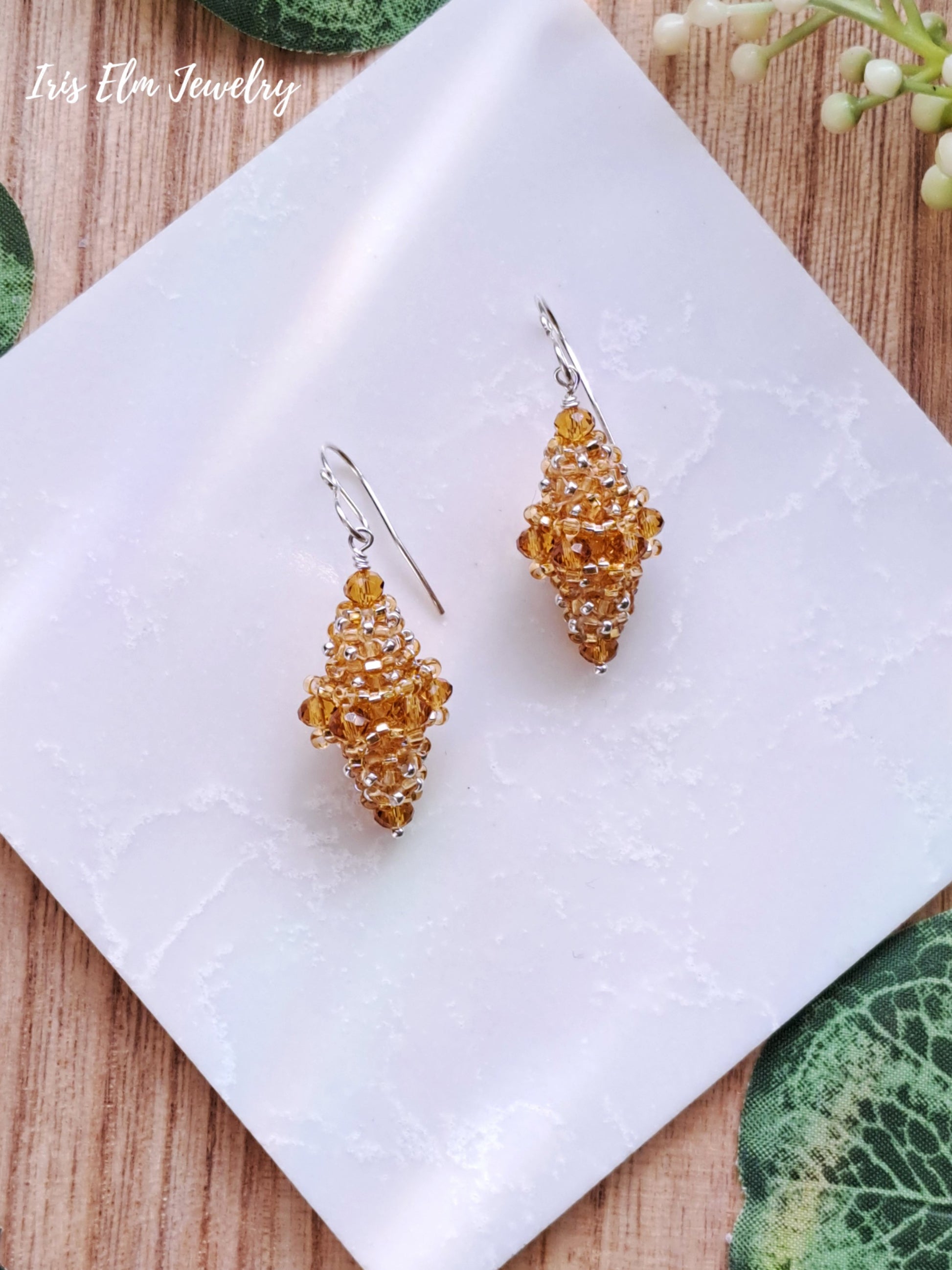 Pair of yellow glass beaded bead earrings on a white tile with a natural wood background