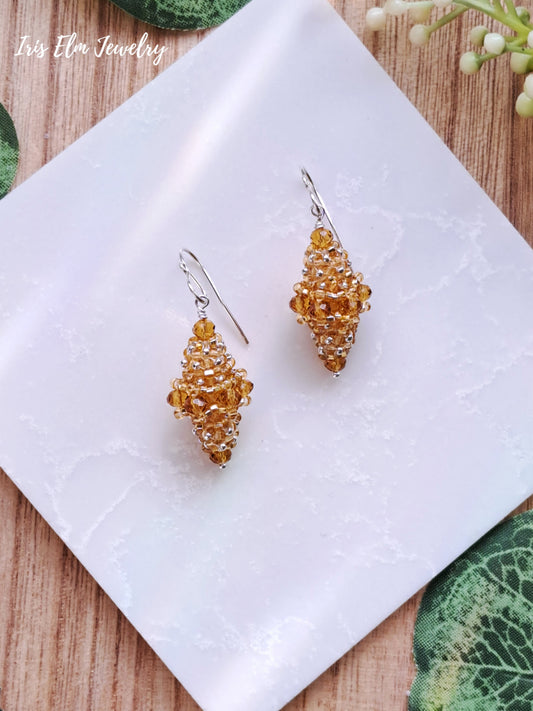 Pair of yellow glass beaded bead earrings on a white tile with a natural wood background