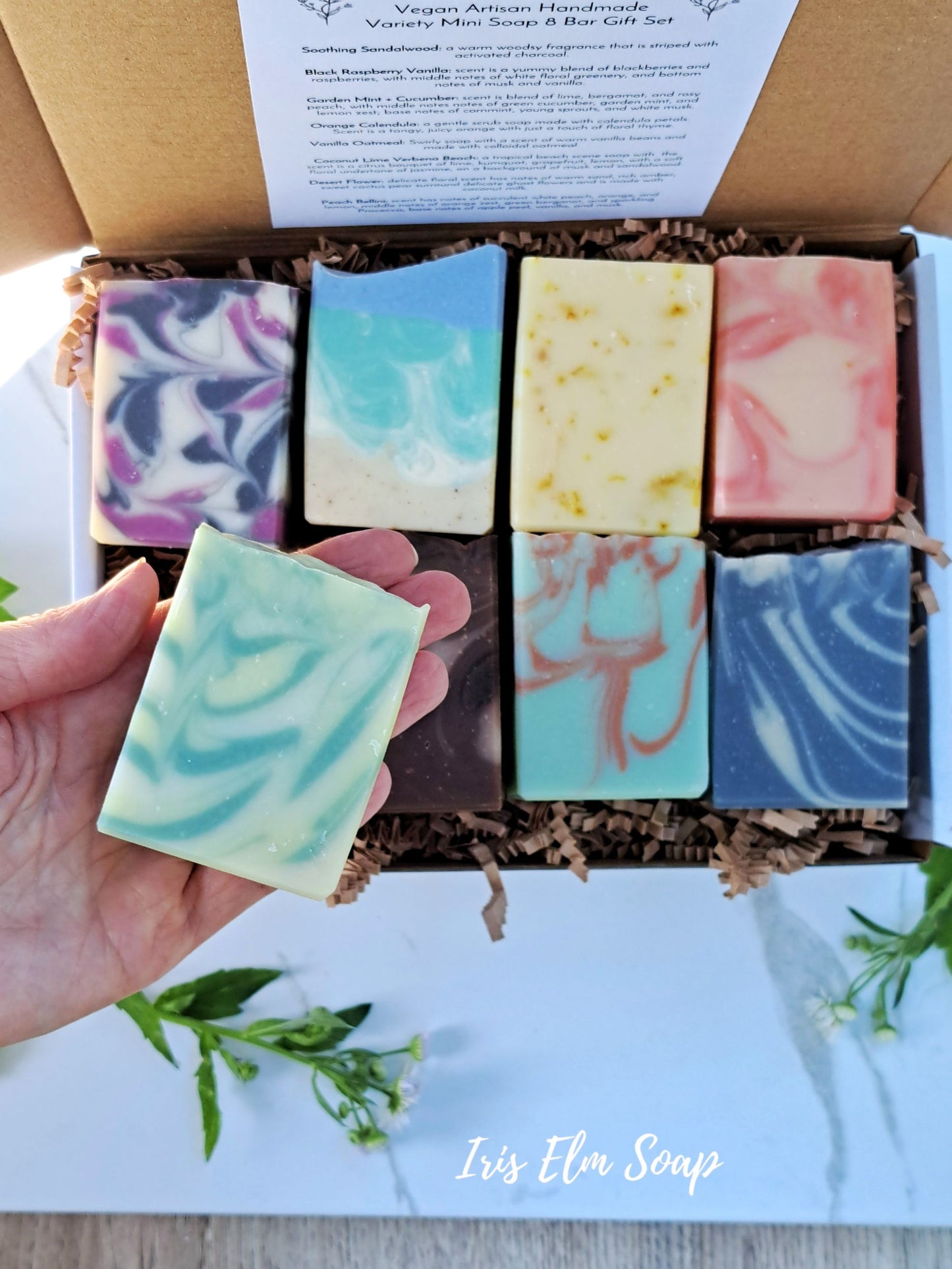 Box of assorted soap bars with a hand holding one, branded 'Iris Elm Soap'.