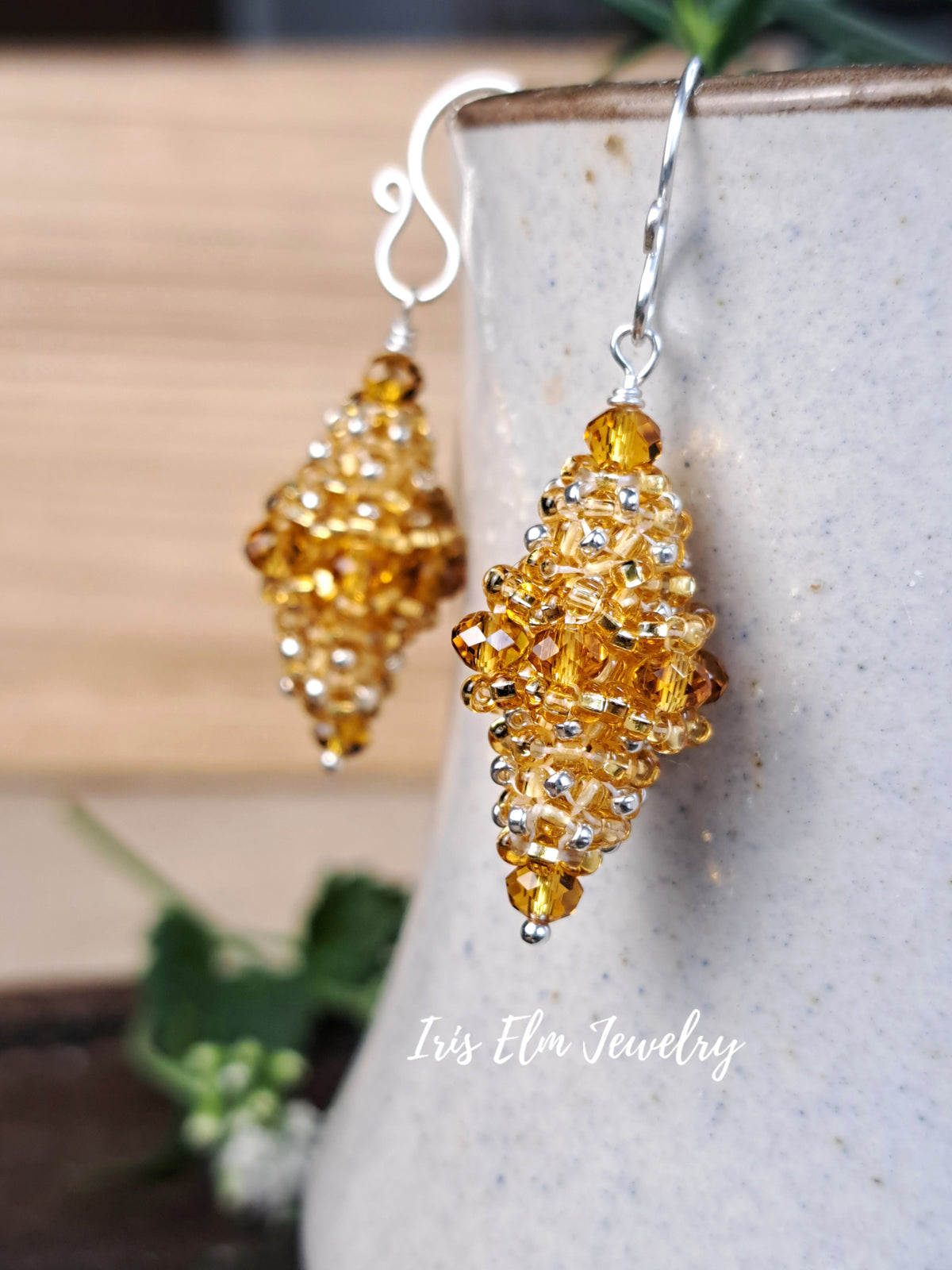 A pair of amber-yellow beaded dangle earrings with silver hooks, displayed on a speckled ceramic vase with a wooden background.