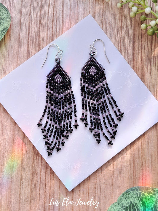 Black beaded seed bead fringe earrings on a white card with a wooden surface background