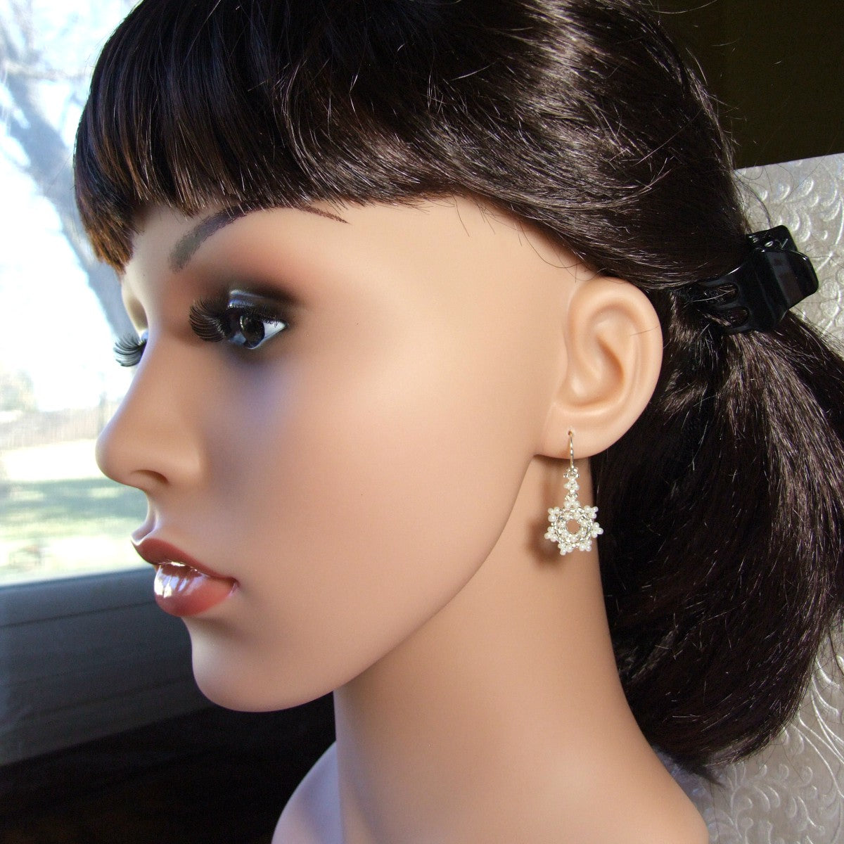 Mannequin head with dark hair styled in a ponytail and wearing small snowflake earrings.