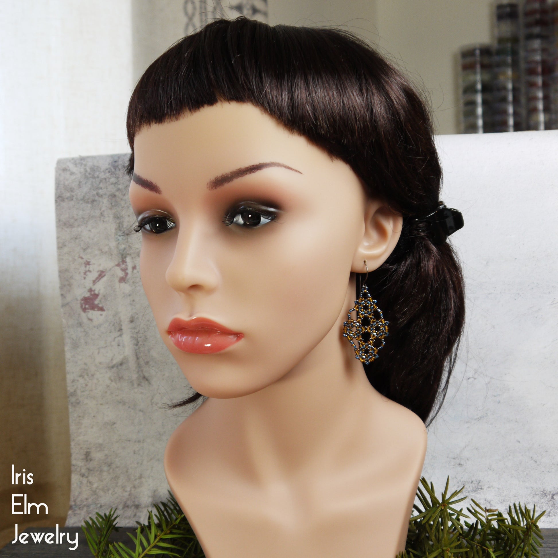 Mannequin head with dark hair and amber orange and blue seed bead lattice earrings on a neutral background