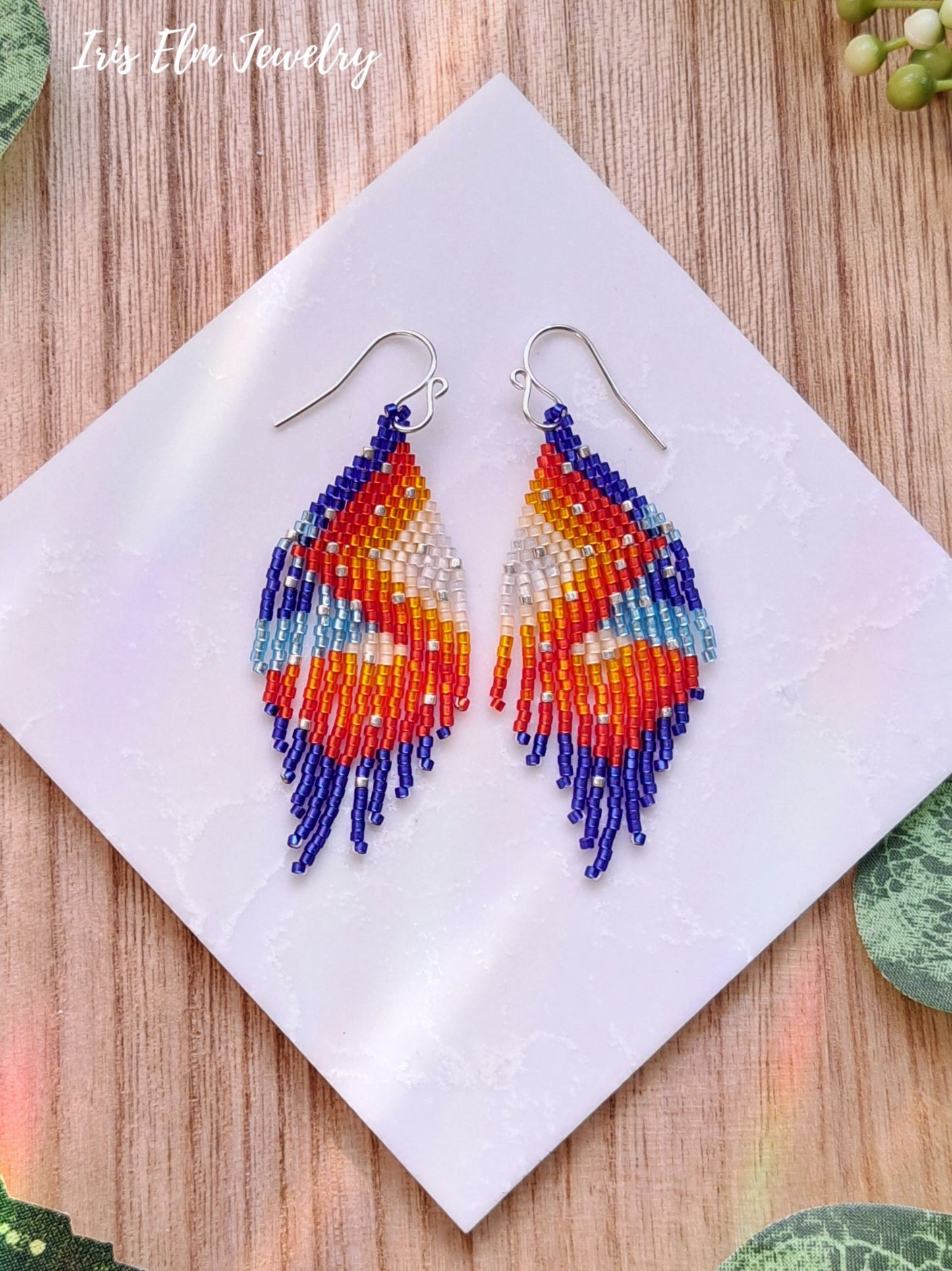 Colorful beaded red orange blue seed bead fringe earrings on a white napkin with 'Iris Elm Jewelry' branding.