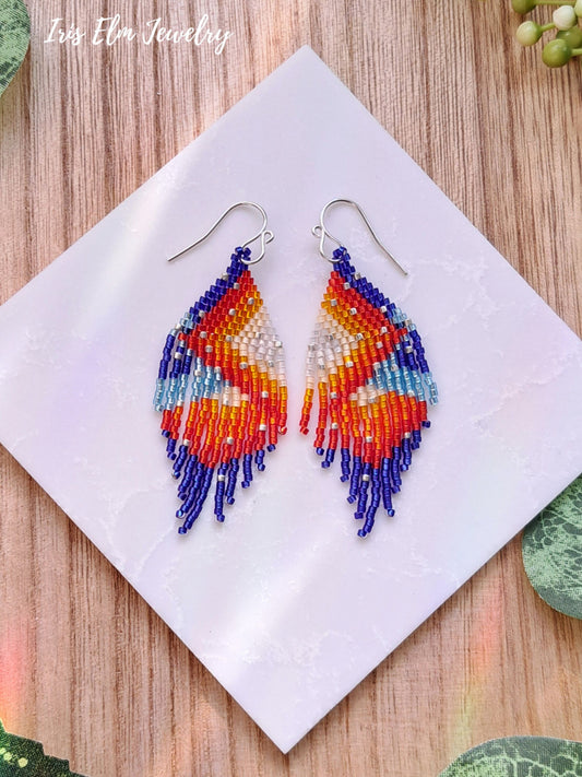 Colorful beaded red orange blue seed bead fringe earrings on a white napkin with 'Iris Elm Jewelry' branding.