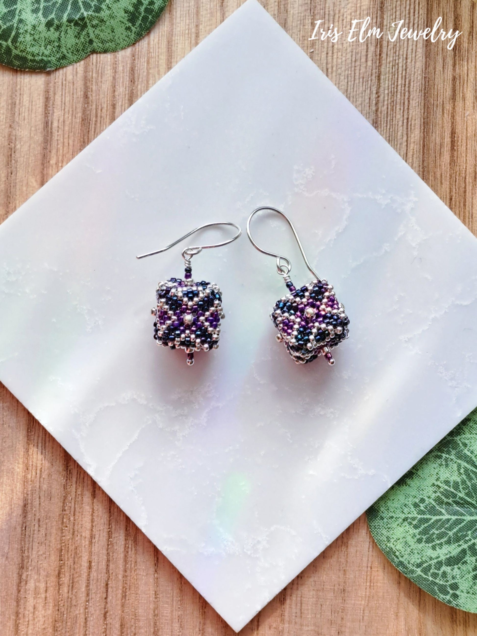 Multicolored beaded purple blue seed bead cube earrings on a white tile with 'Iris Elm Jewelry' branding.