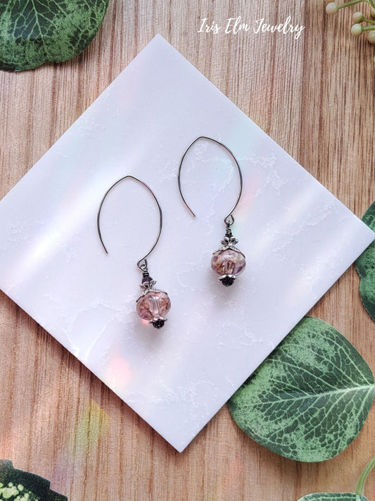 Pair of earrings with purple wildflowers and beads on a white napkin with 'Iris Elm Jewelry' branding.