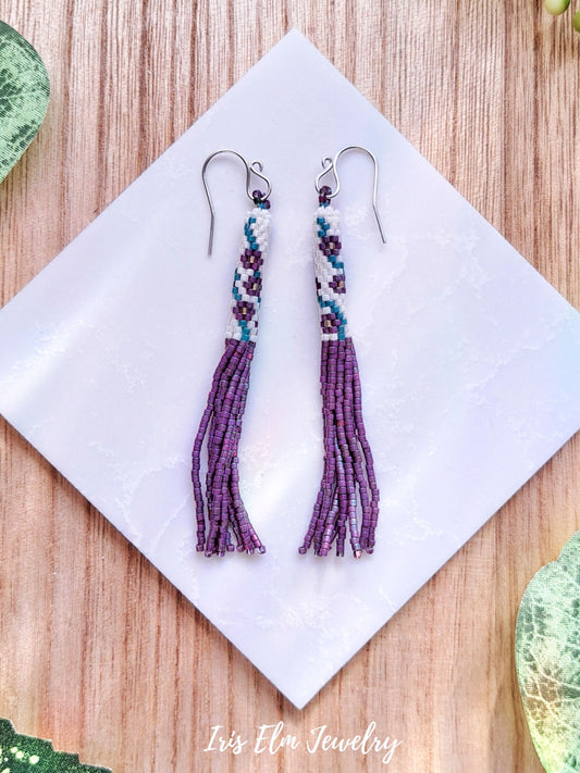 Pair of beaded tassel pink purple seed bead flower earrings on a white napkin with 'Iris Elm Jewelry' branding.